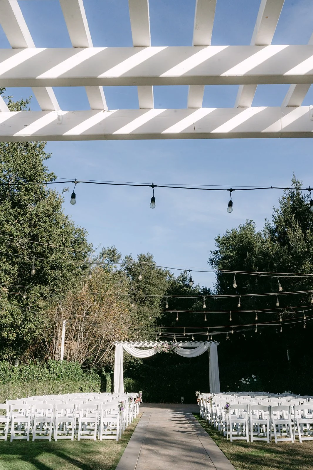 The ceremony aisle leading to the white pergola under string lights.