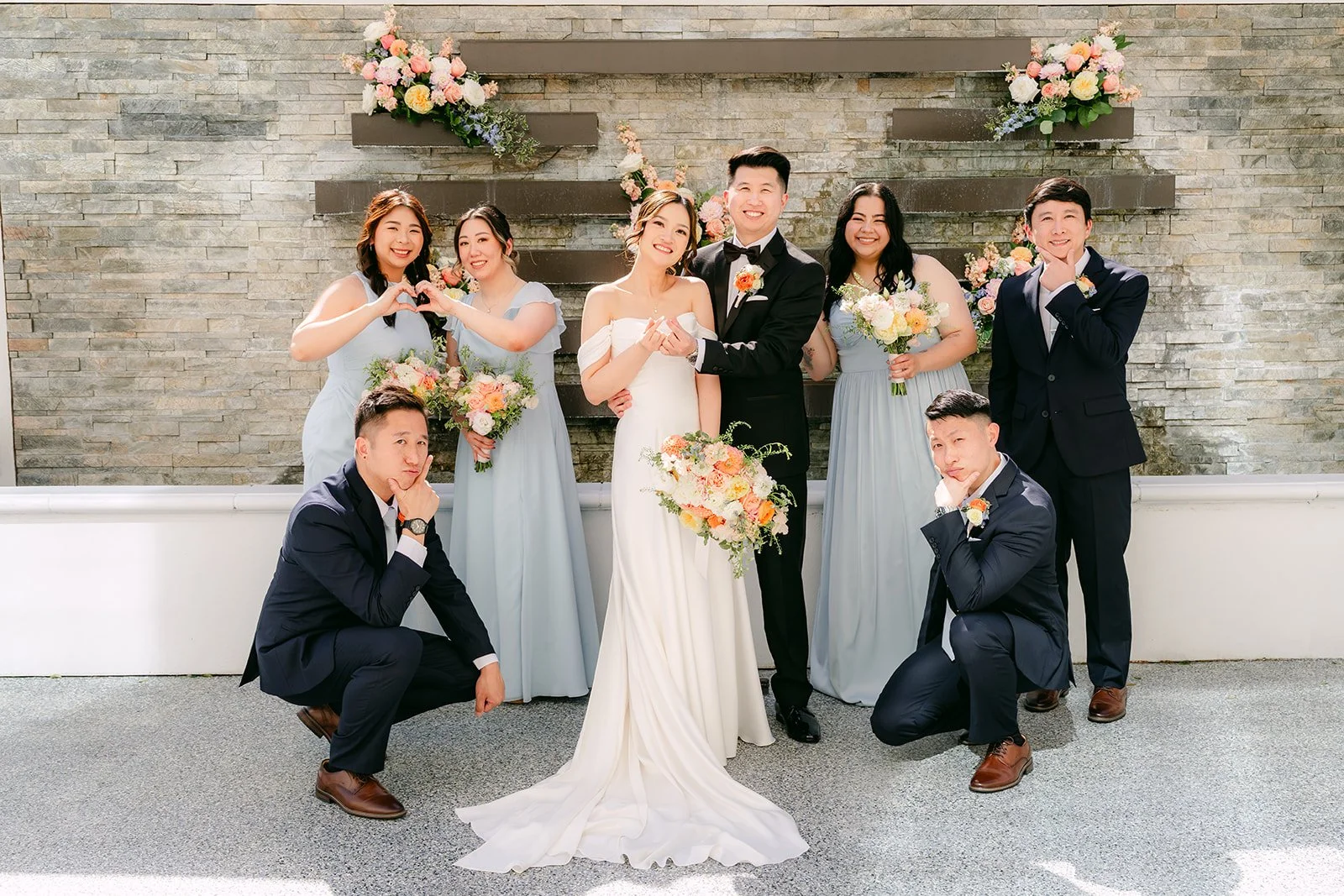 The groomsmen kneeling in front of Amanda, San and the bridesmaids.