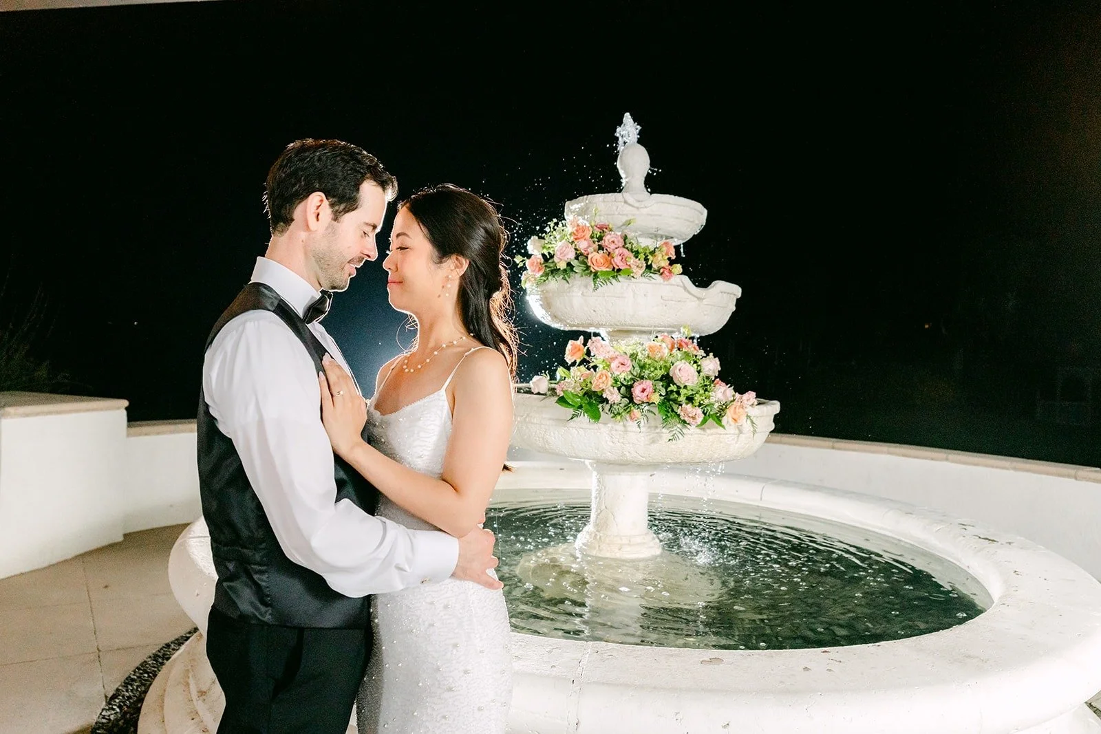 Stephanie and Kevin embracing by the lit fountain at night