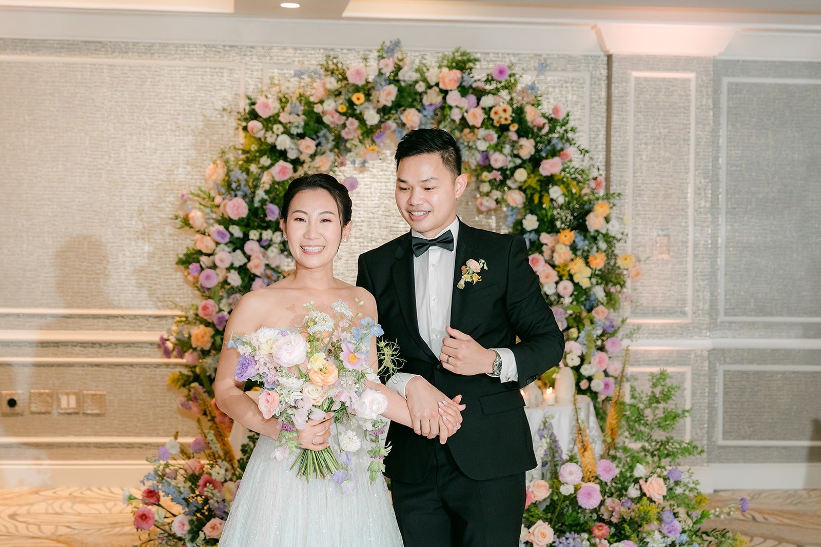 Kylie and Mario smiling in front of the floral arch in the ballroom