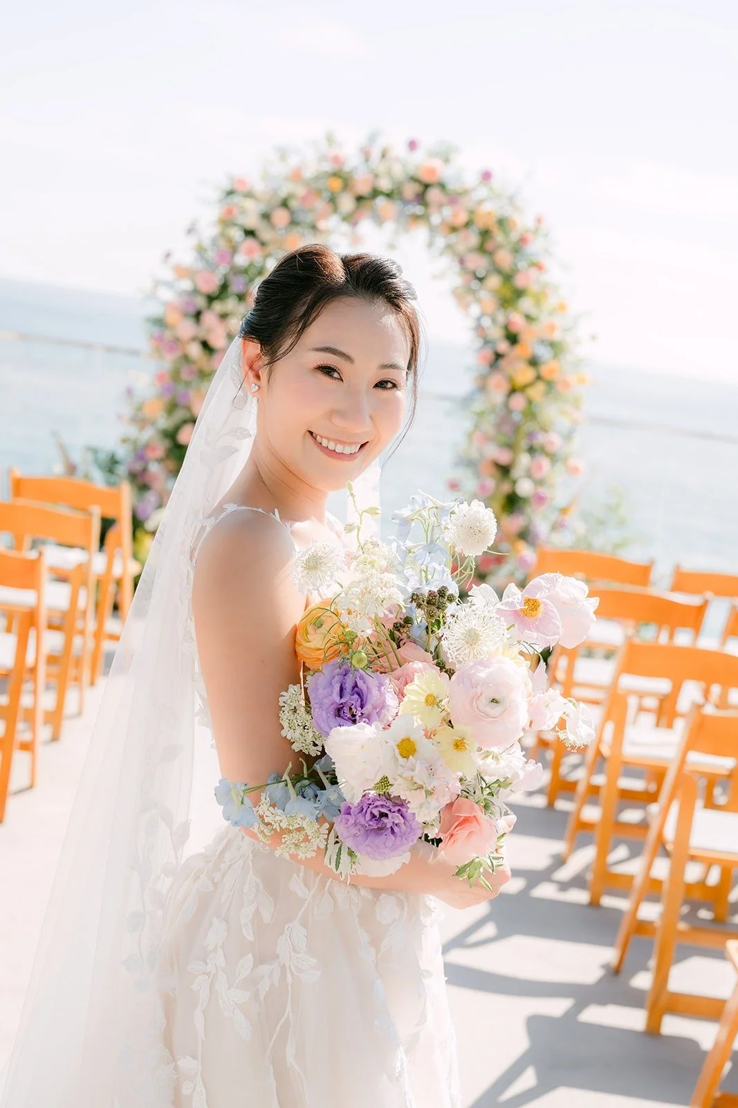 Kylie with her bouquet in front of the floral arch on the terrace, photographed by One and Only Production