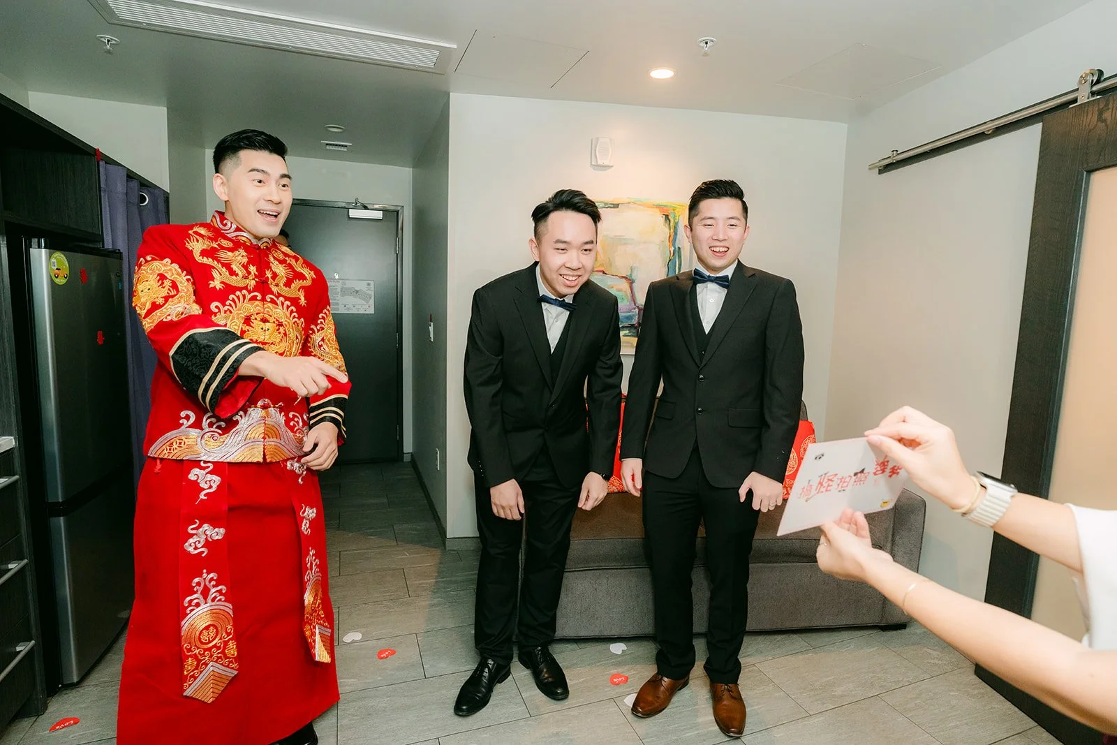 A groom in a red changshan and his groomsmen waiting outside the hotel suite door.