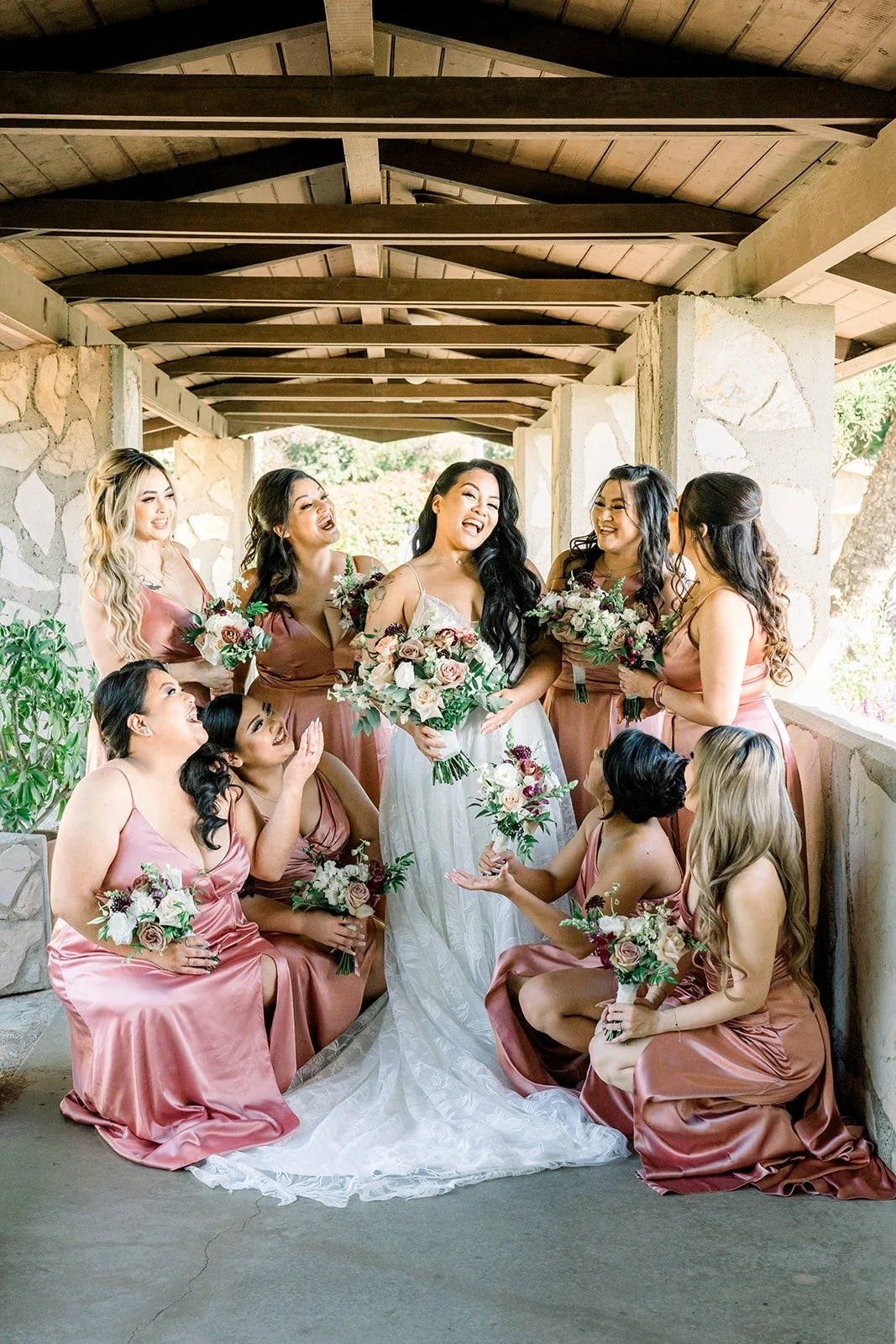 The bridesmaids gather around Betsy under a wooden covered walkway
