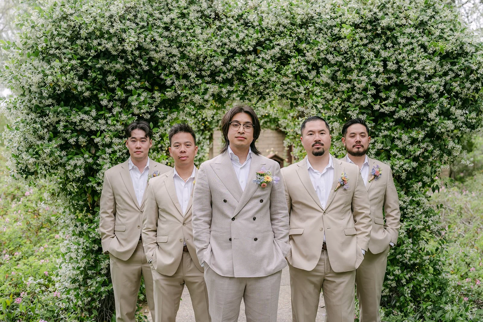 Mike with his groomsmen in beige suits in front of an ivy hedge