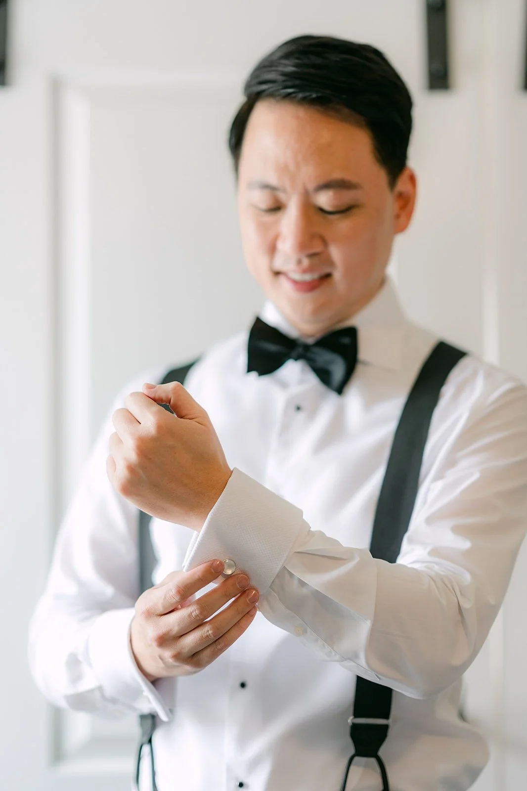 William fastening his cufflinks in a white shirt and suspenders