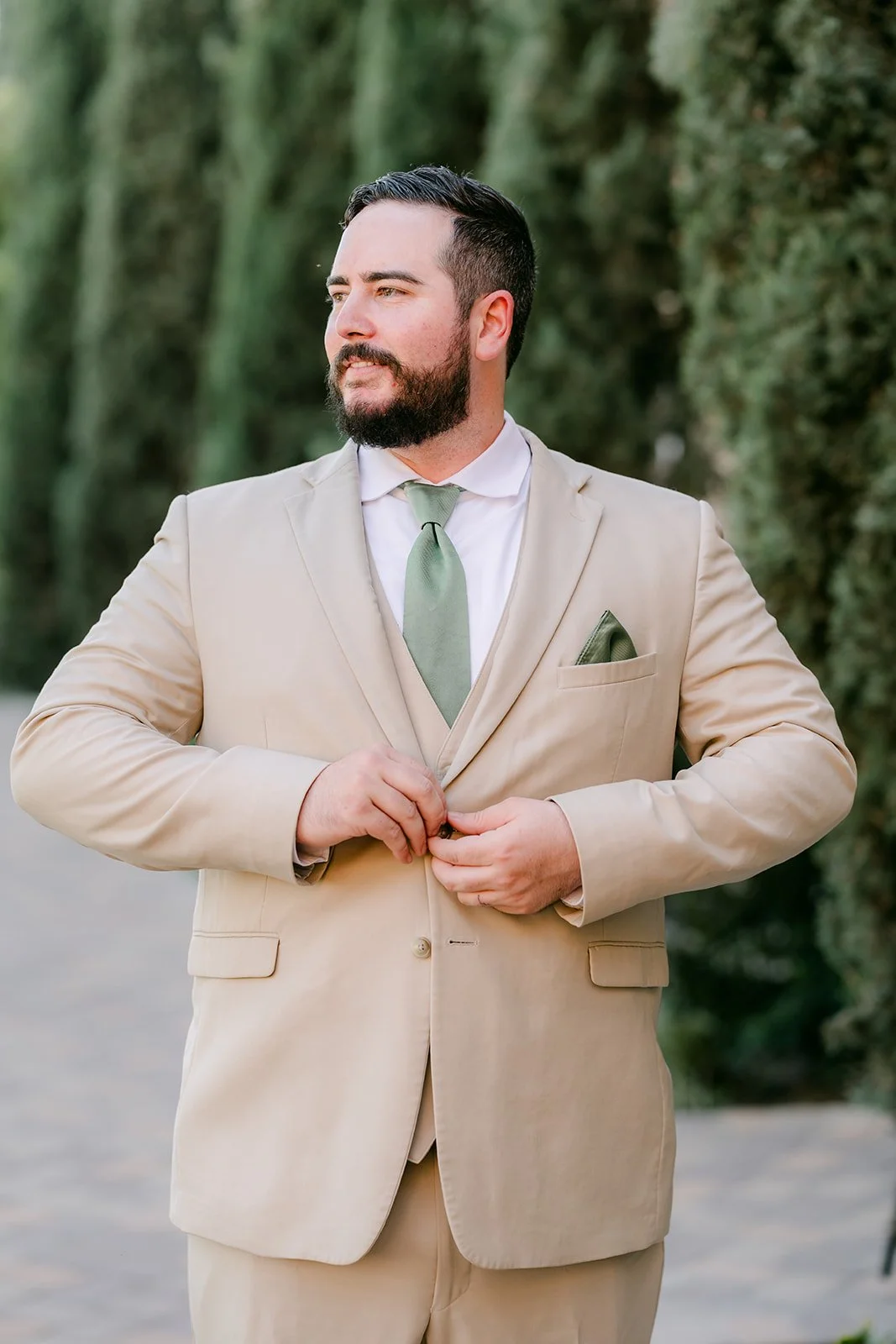 Cody buttoning his tan suit jacket.