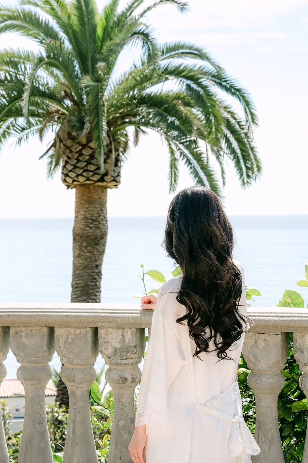 Bride with long curls looking out at palm trees and the ocean