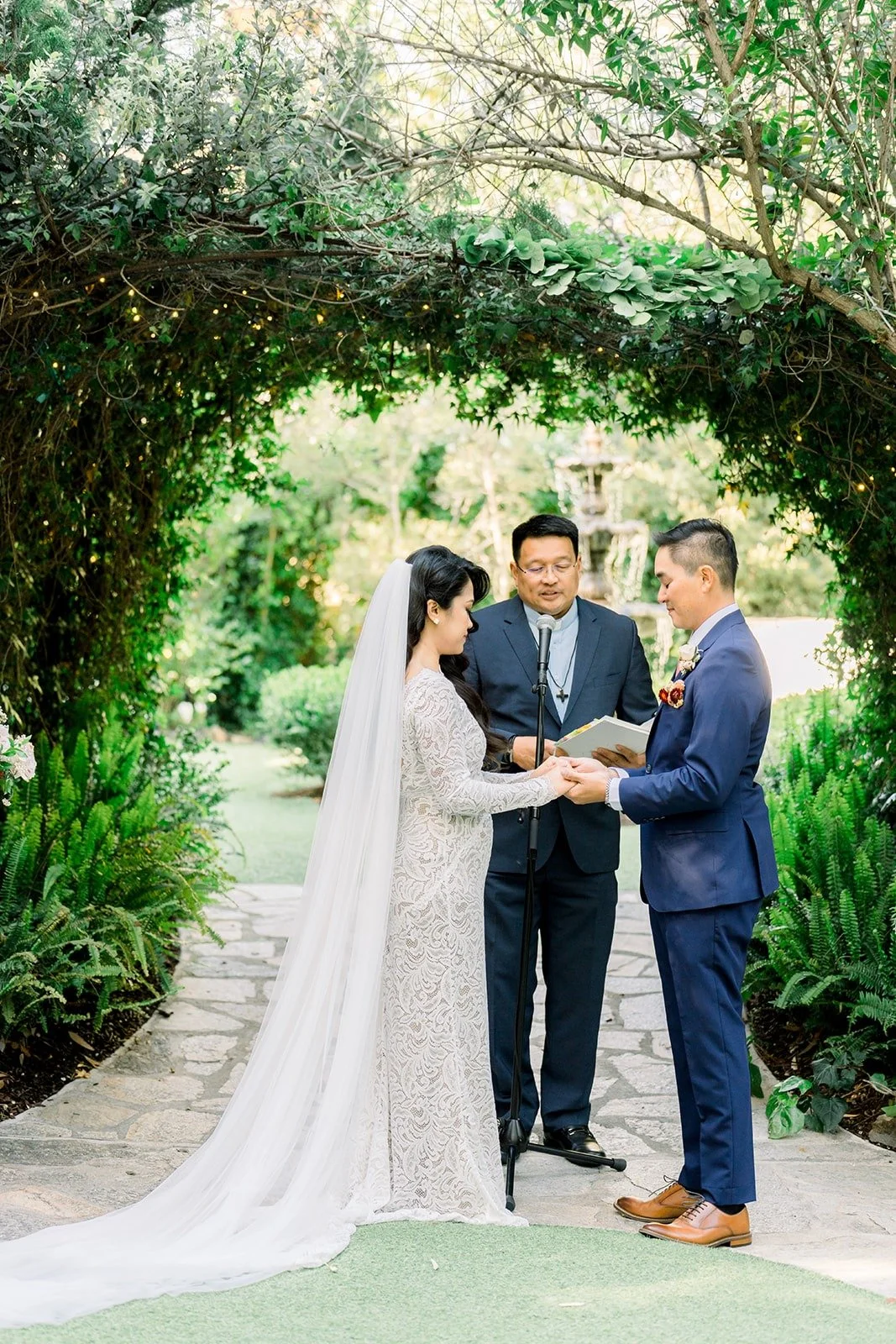 Hannah and Vincent under the green arbor during the ceremony