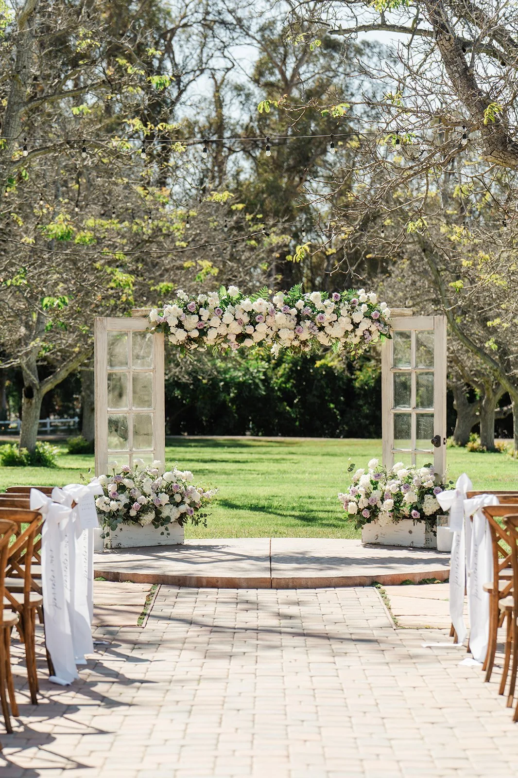 Ceremony aisle with white wooden doors and floral arch under the walnut trees