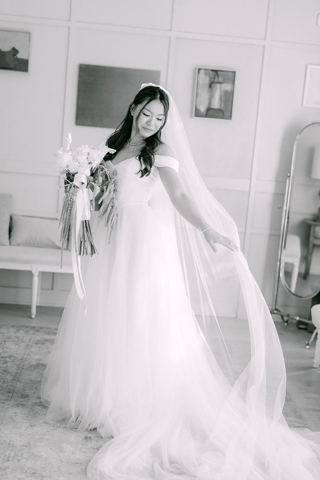 Black and white photo of Jadee and her long train in the bridal suite, photographed by One and Only Production