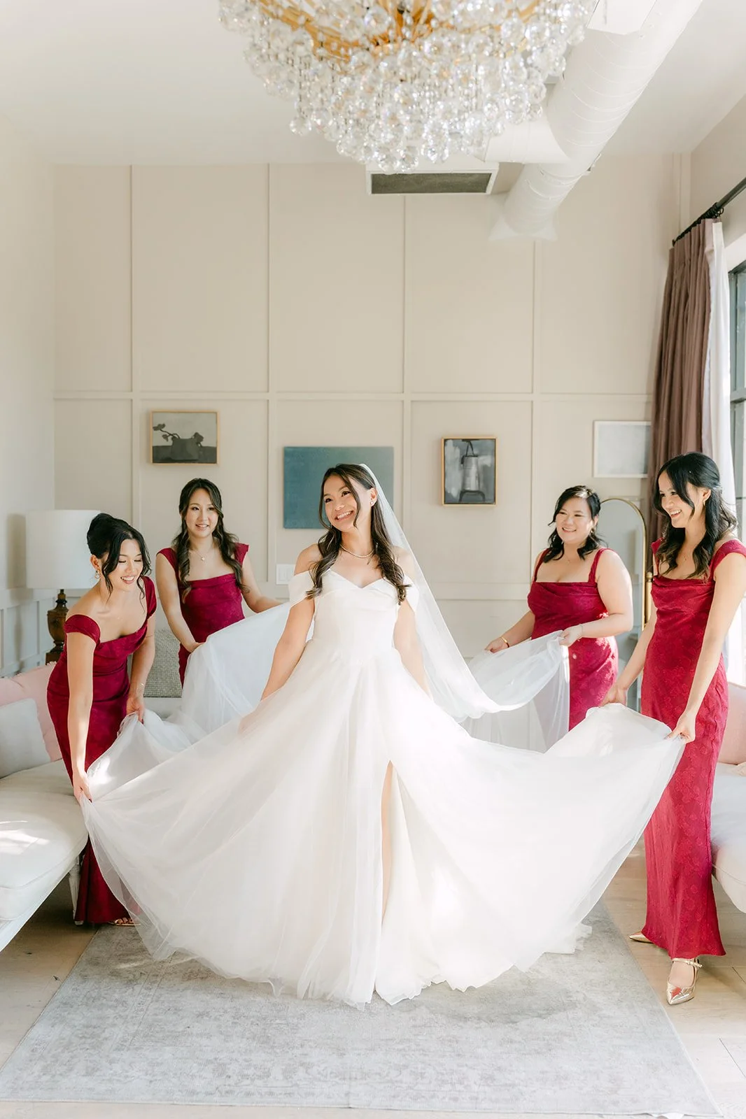 Bridesmaids in burgundy fanning out Jadee's train under the chandelier
