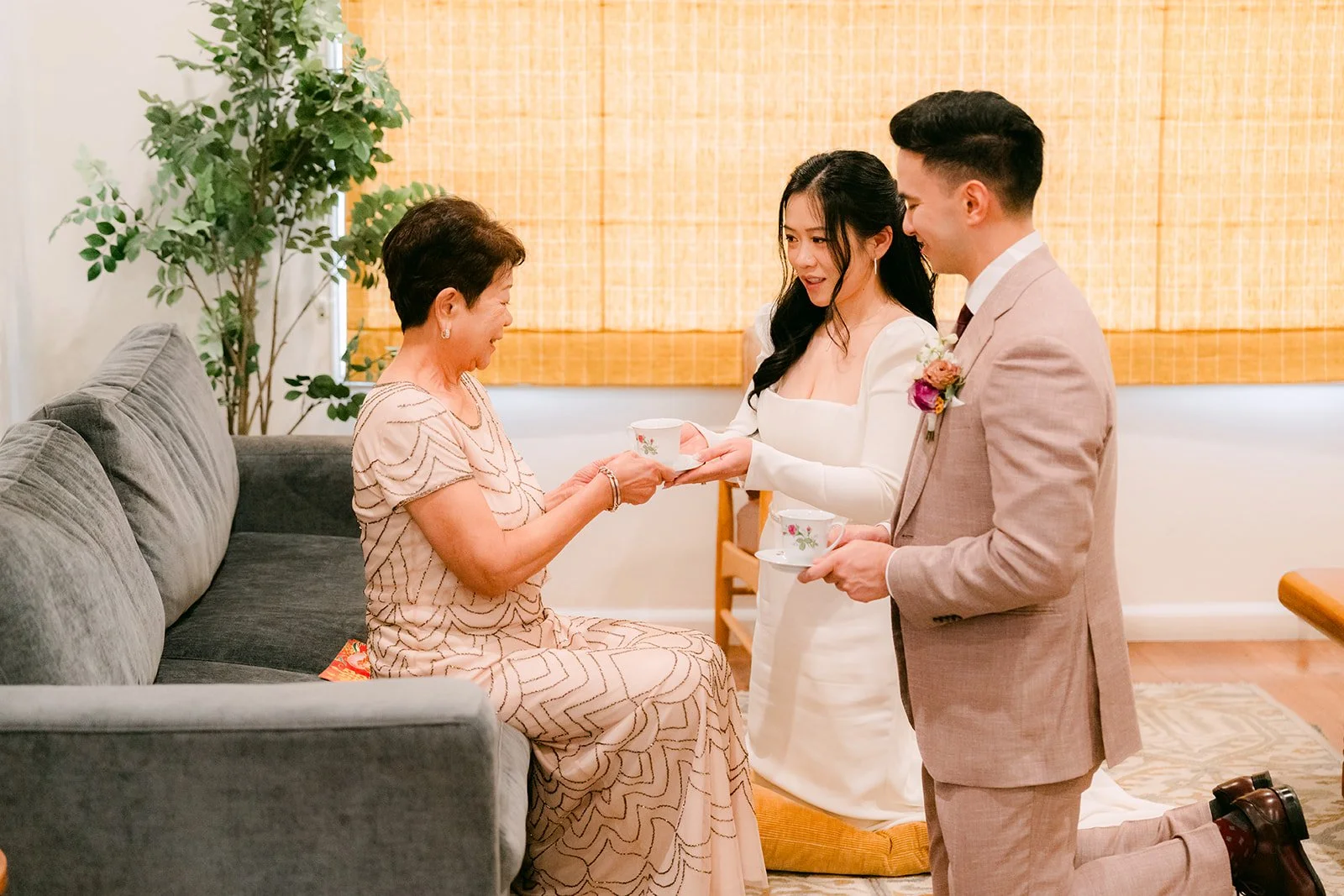 Denise and Michael offering tea to her mom on the sofa.