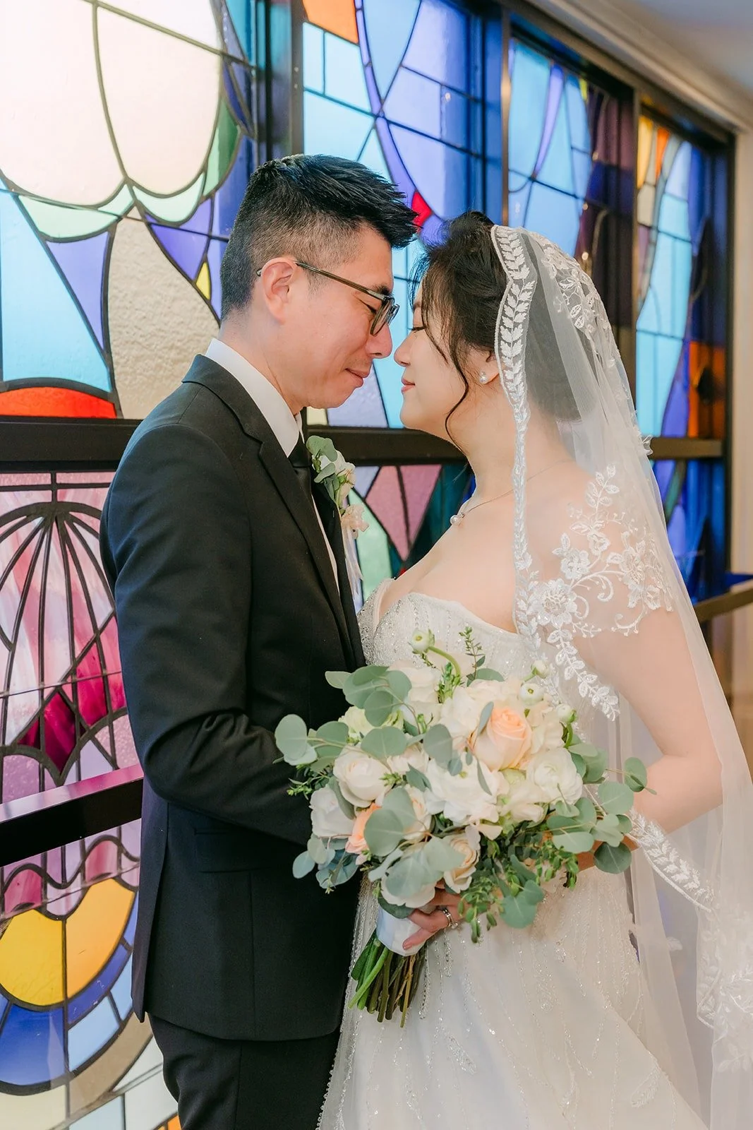 Eunice and Eric face each other in front of the colorful stained glass
