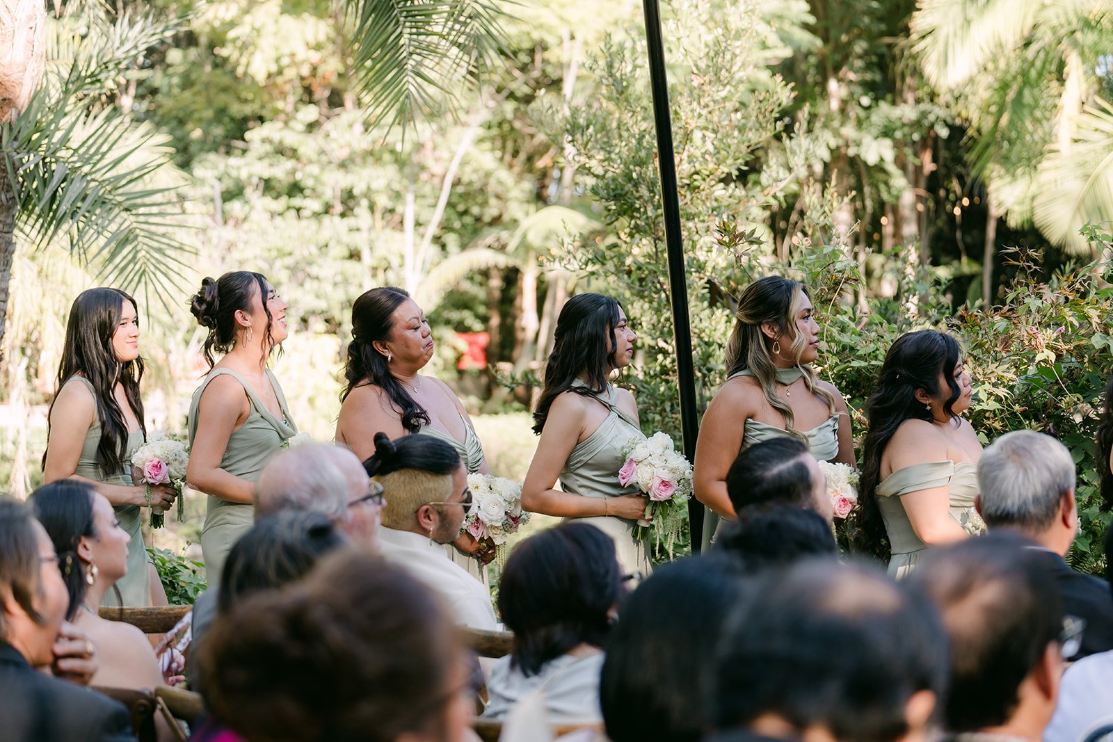 Guests and bridesmaids watching Nicole and Caryl's ceremony among the palms.