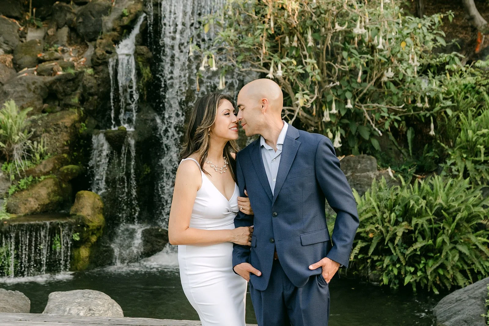 Francesca and Daniel stand together by the waterfall and pond.