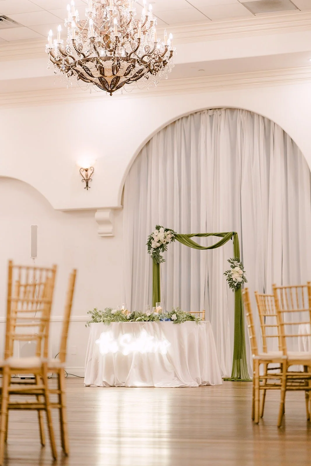 Sweetheart table under a greenery arch in the ballroom
