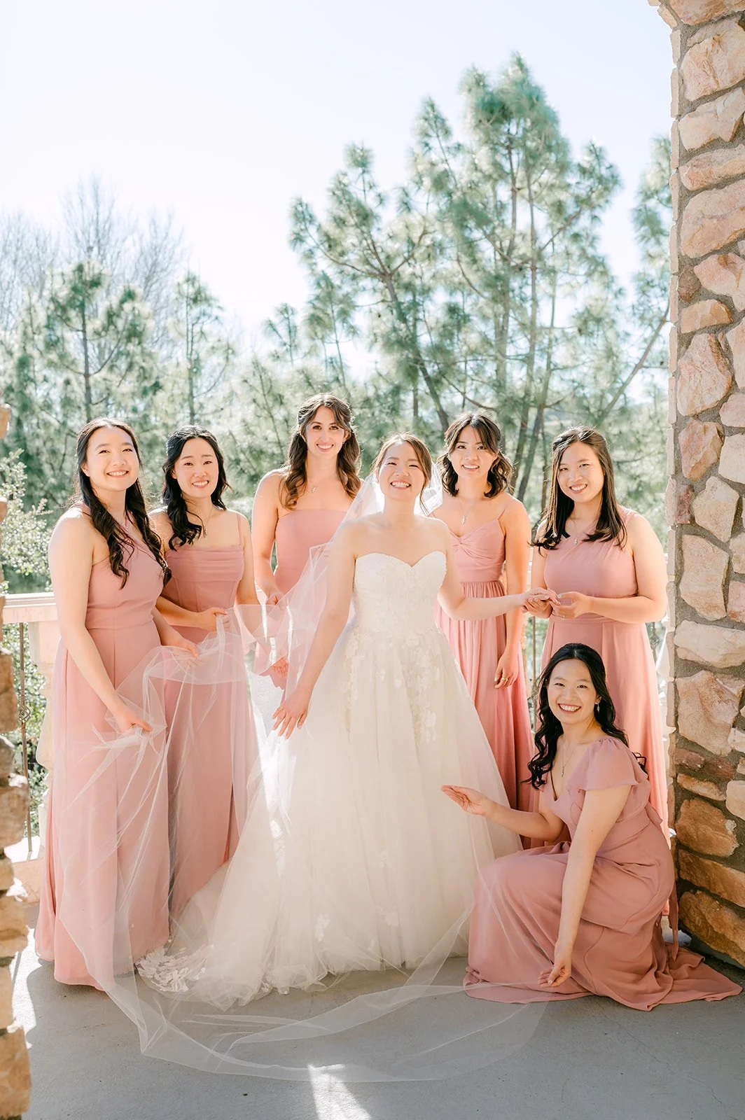 Bride with her bridesmaids in dusty rose gowns on the balcony
