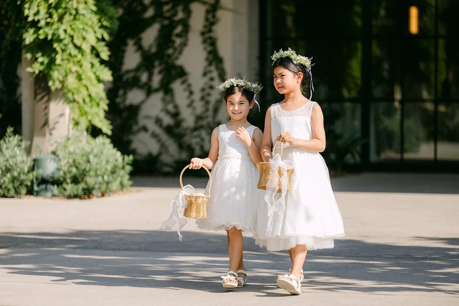 Flower girls in white dresses with floral crowns carrying baskets