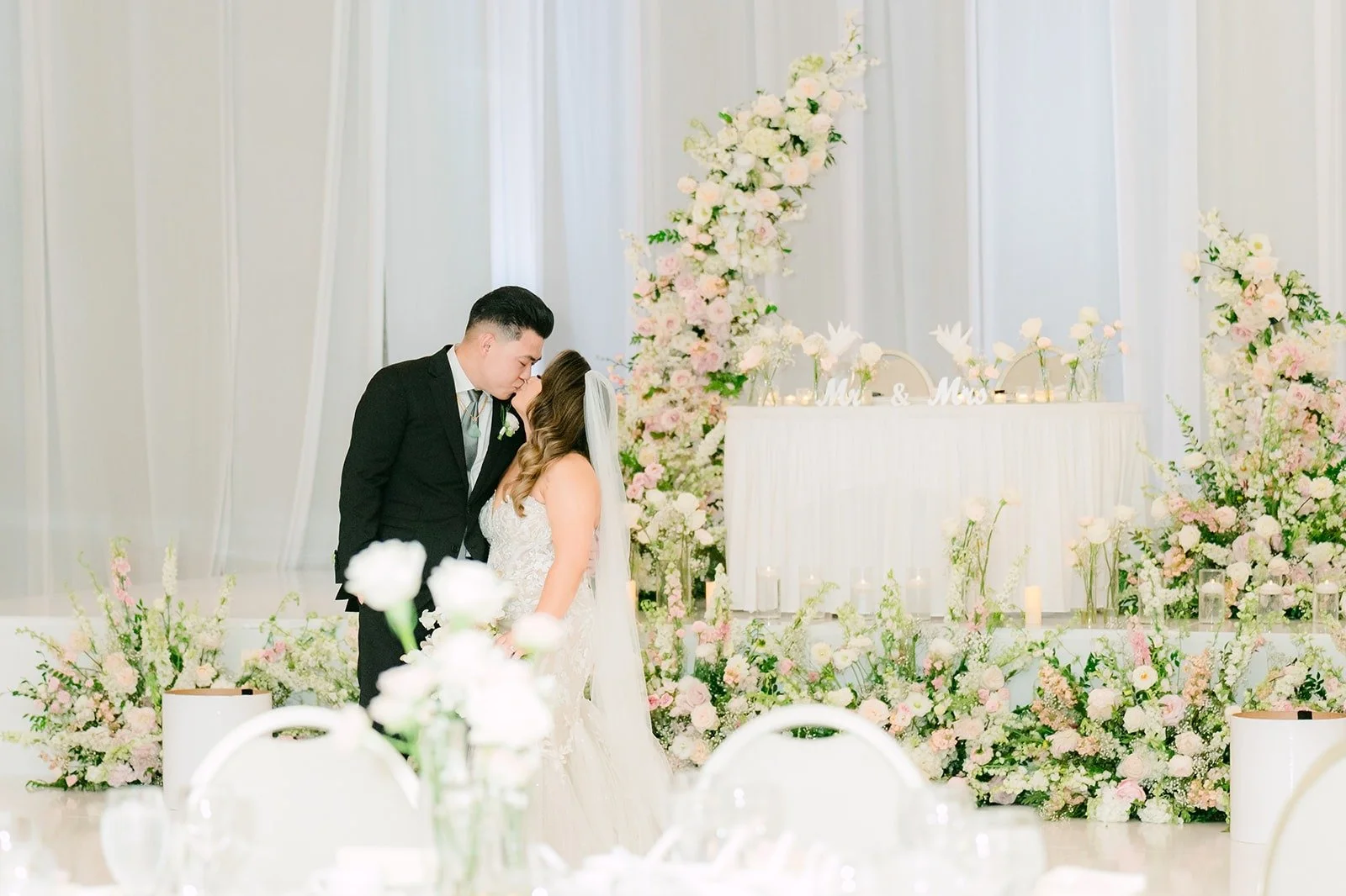 Candice and Vincent kissing beside the floral sweetheart table