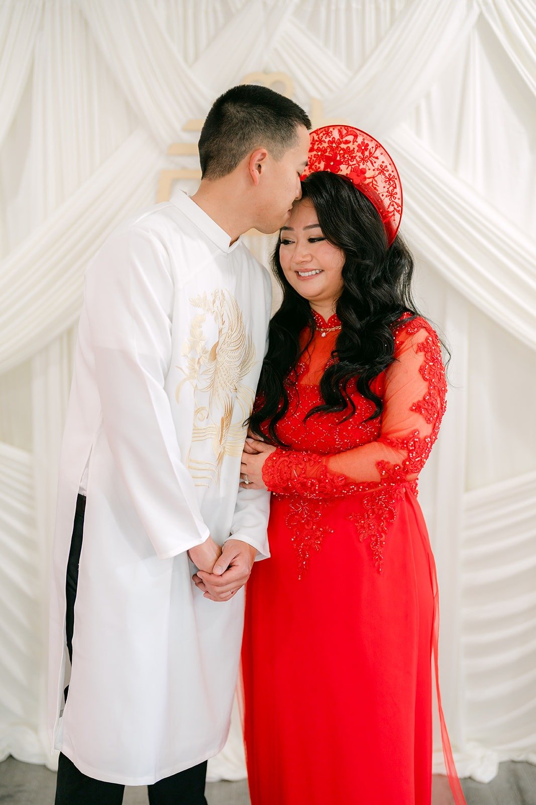 Kevin kisses Jennifer's forehead in their red and white ao dai