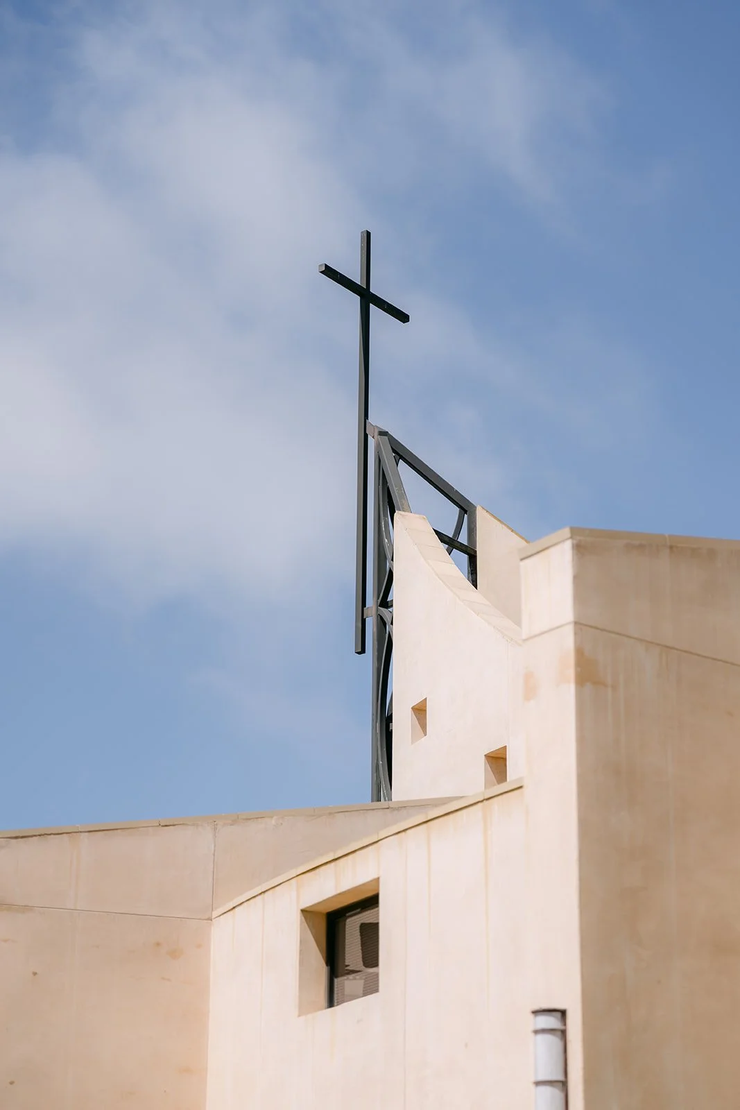 The cross atop St. John Fisher Church against a blue sky