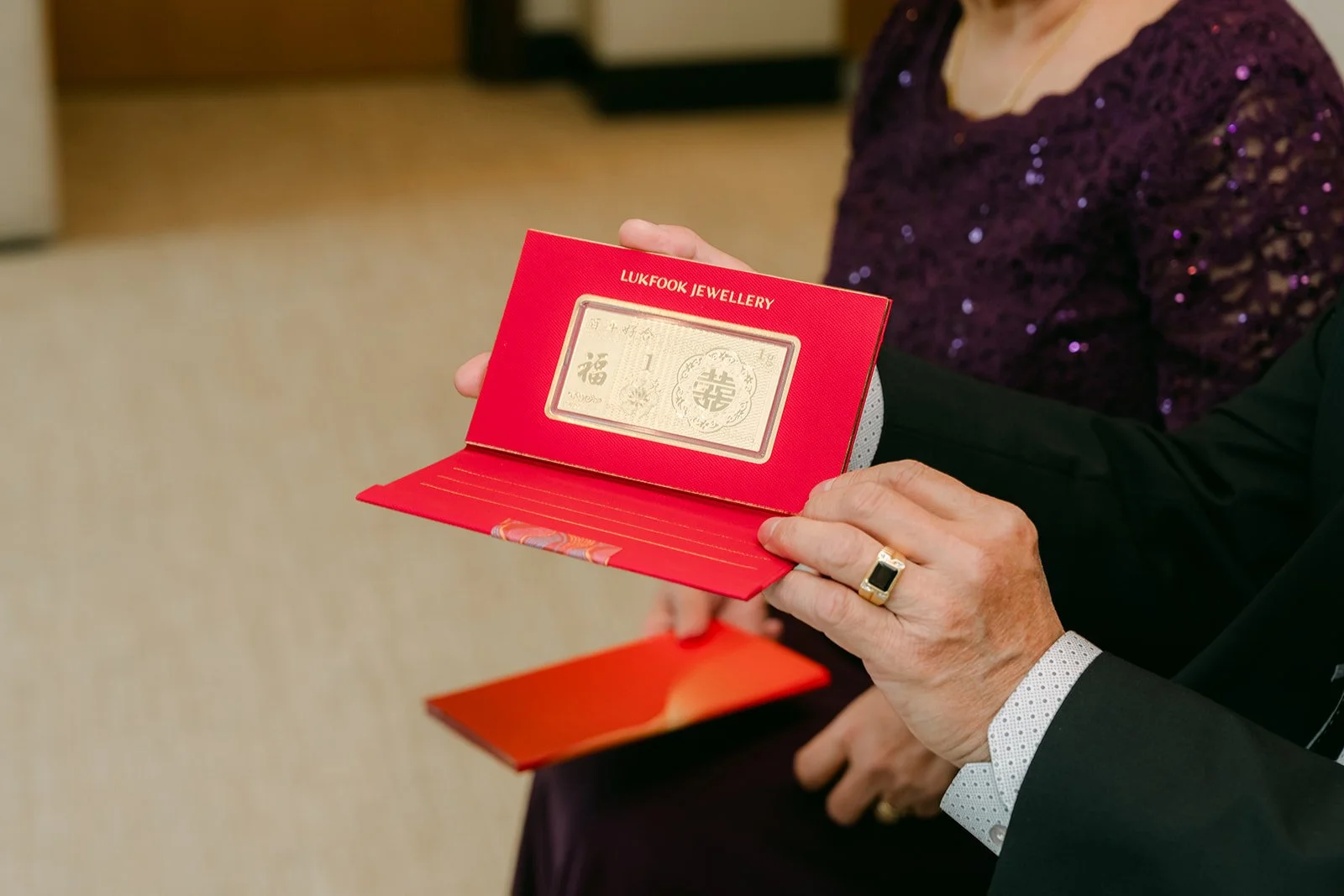 A relative presenting a red gift card holding gold to the couple.