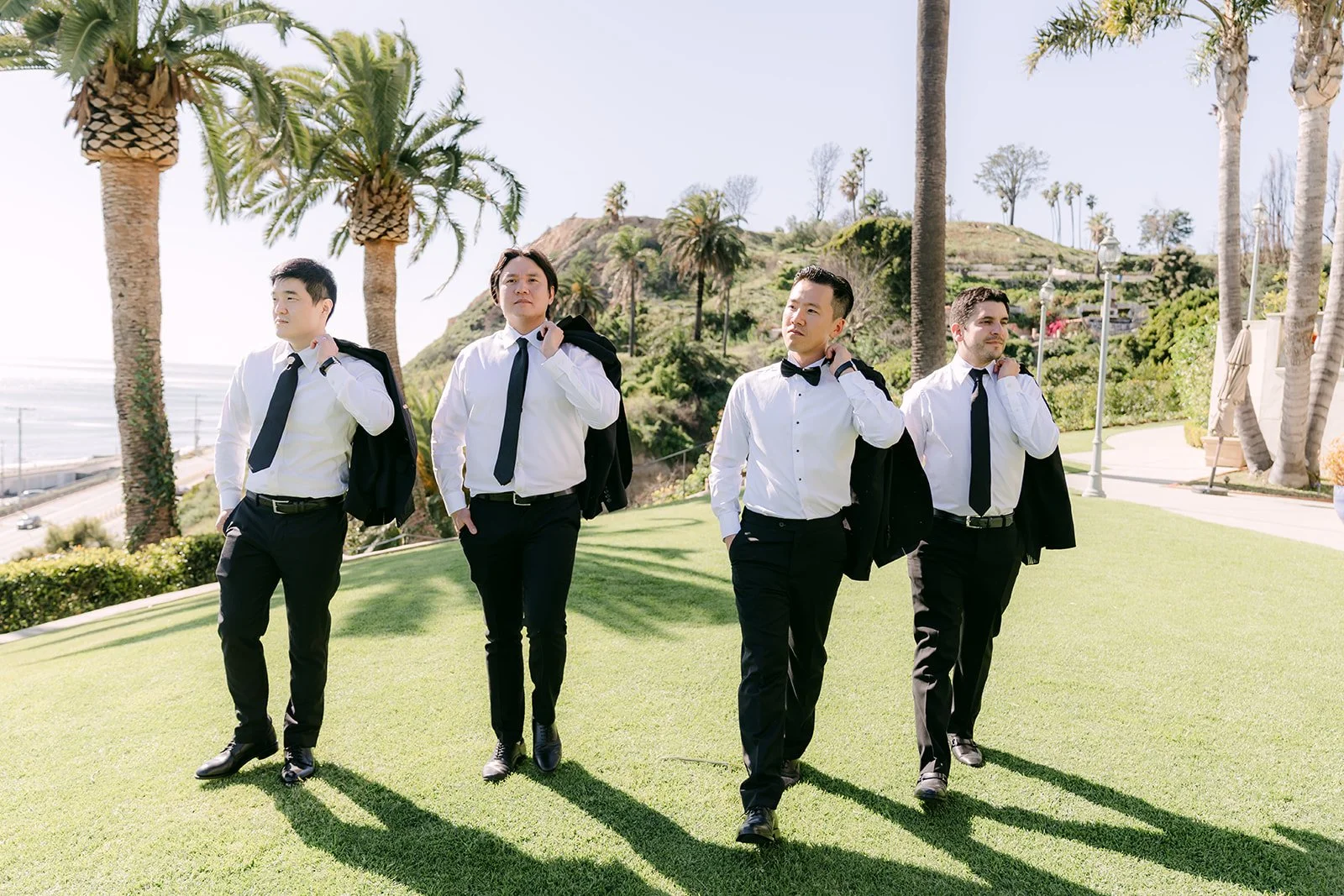 Groomsmen walking across the lawn with jackets over their shoulders