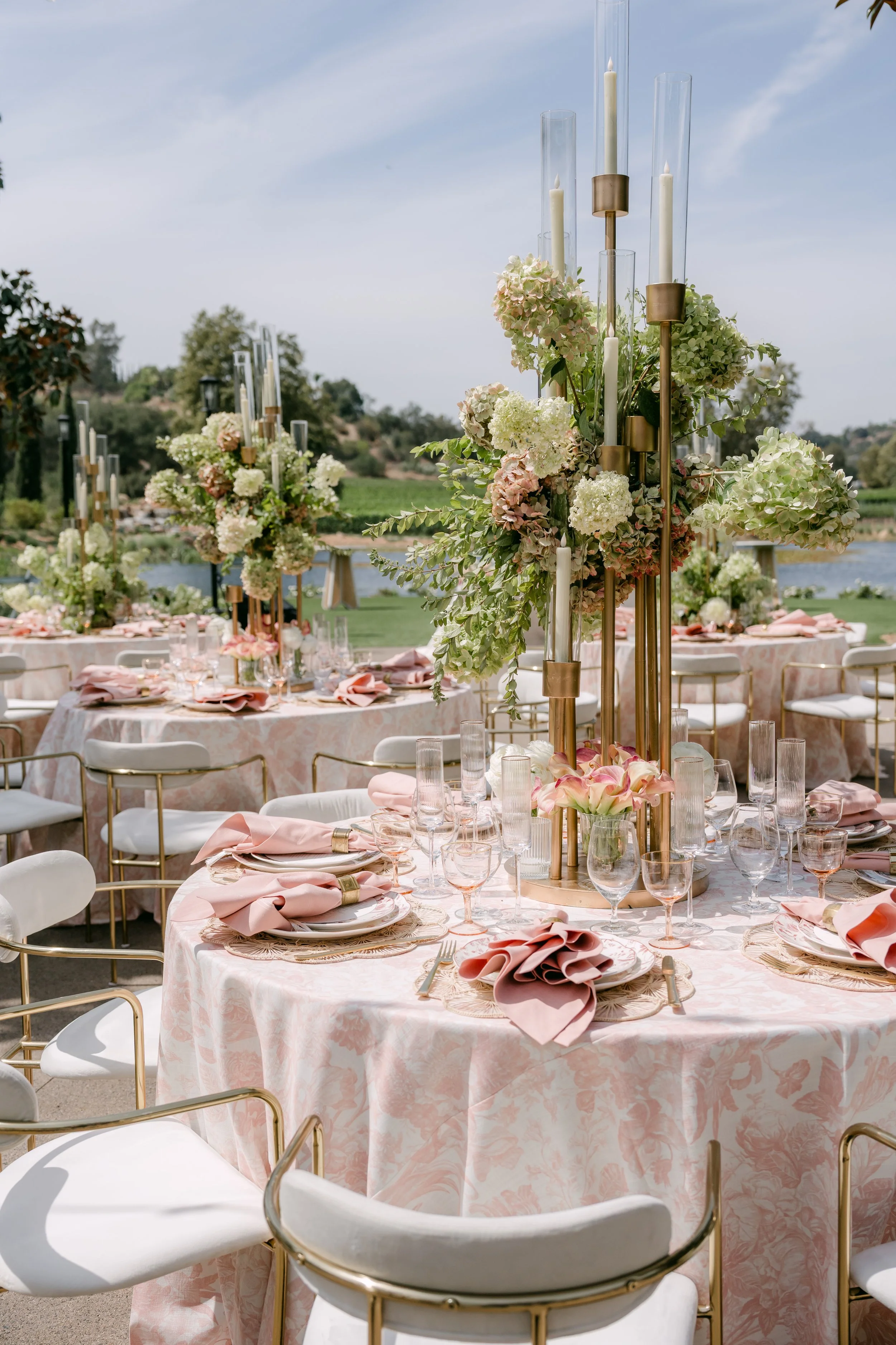 Reception tables with pink linens and tall hydrangea centerpieces by the lake at Monserate Winery