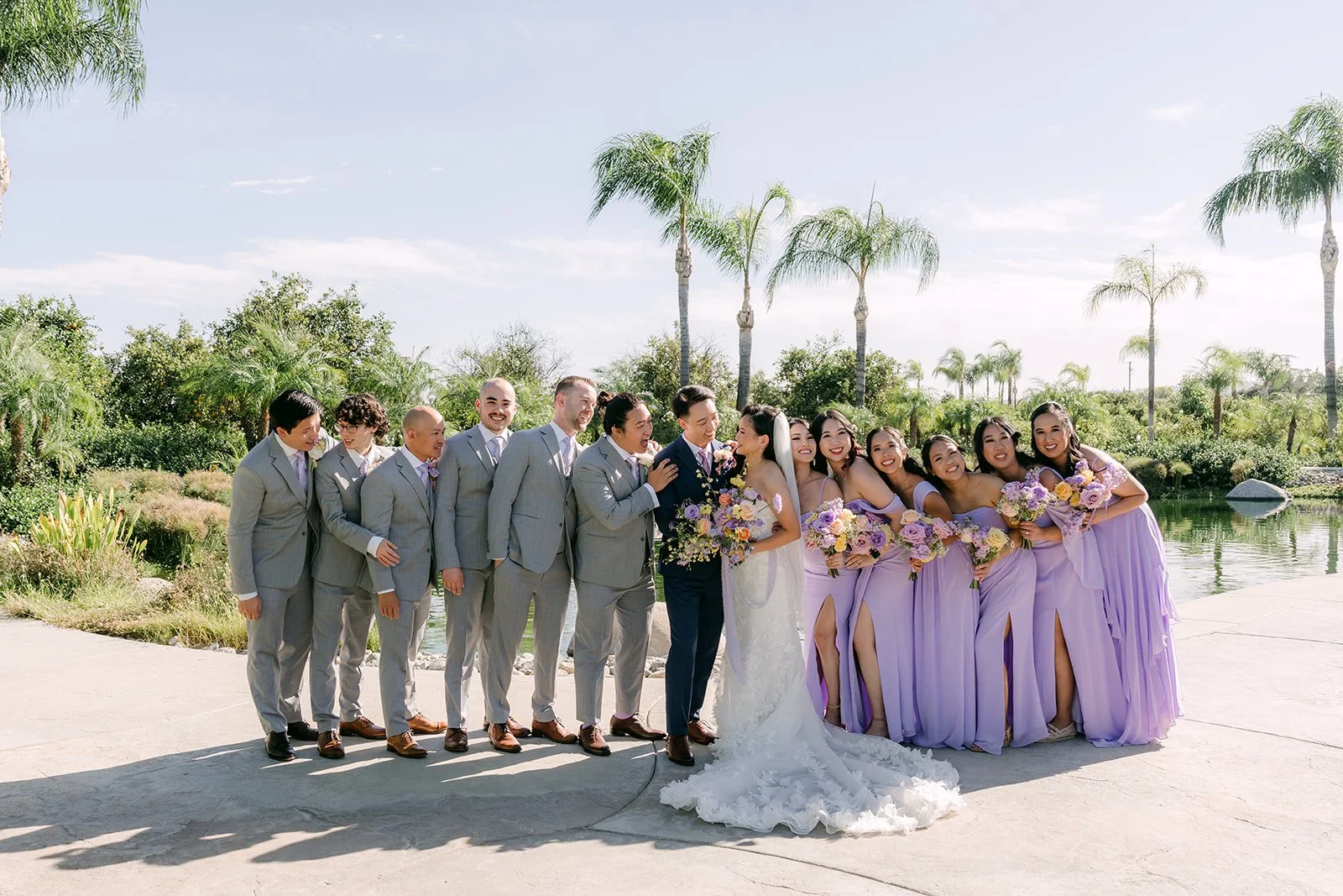 The full wedding party by the pond with palms and mountains behind them.