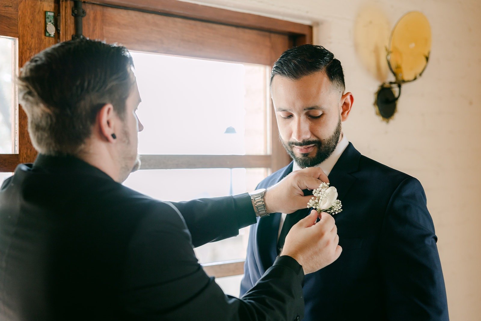 A friend pinning Danny's boutonniere by the window