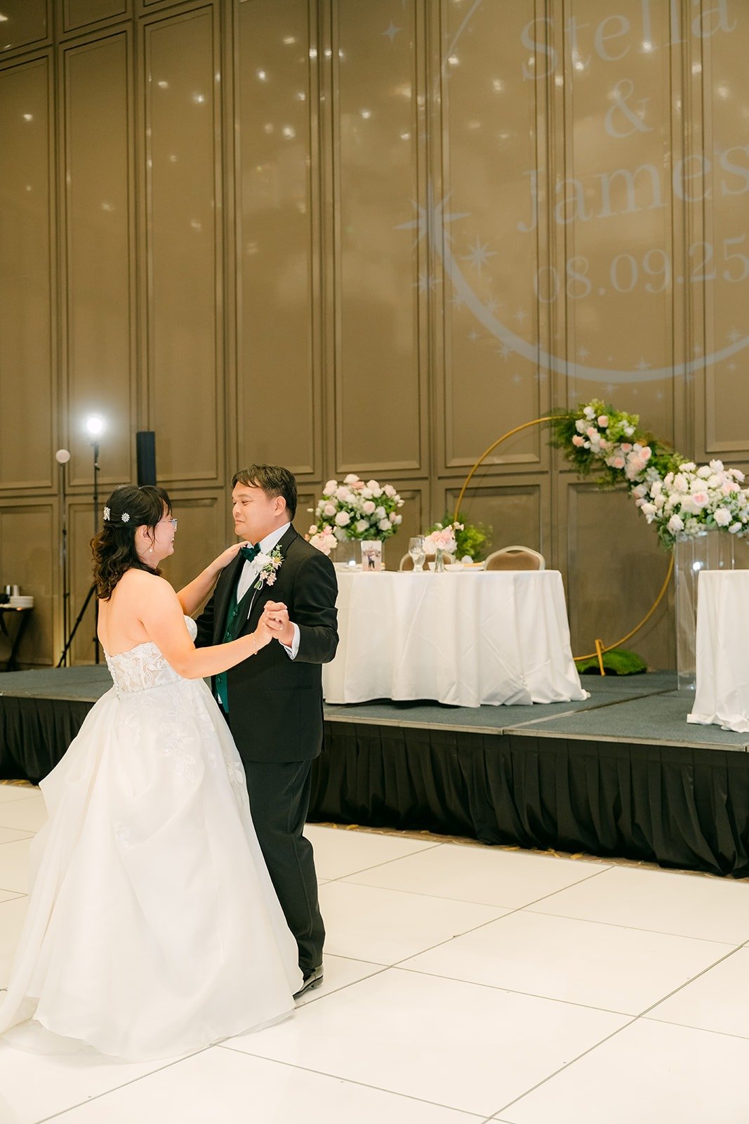 Stella and James dancing close in front of the sweetheart table florals