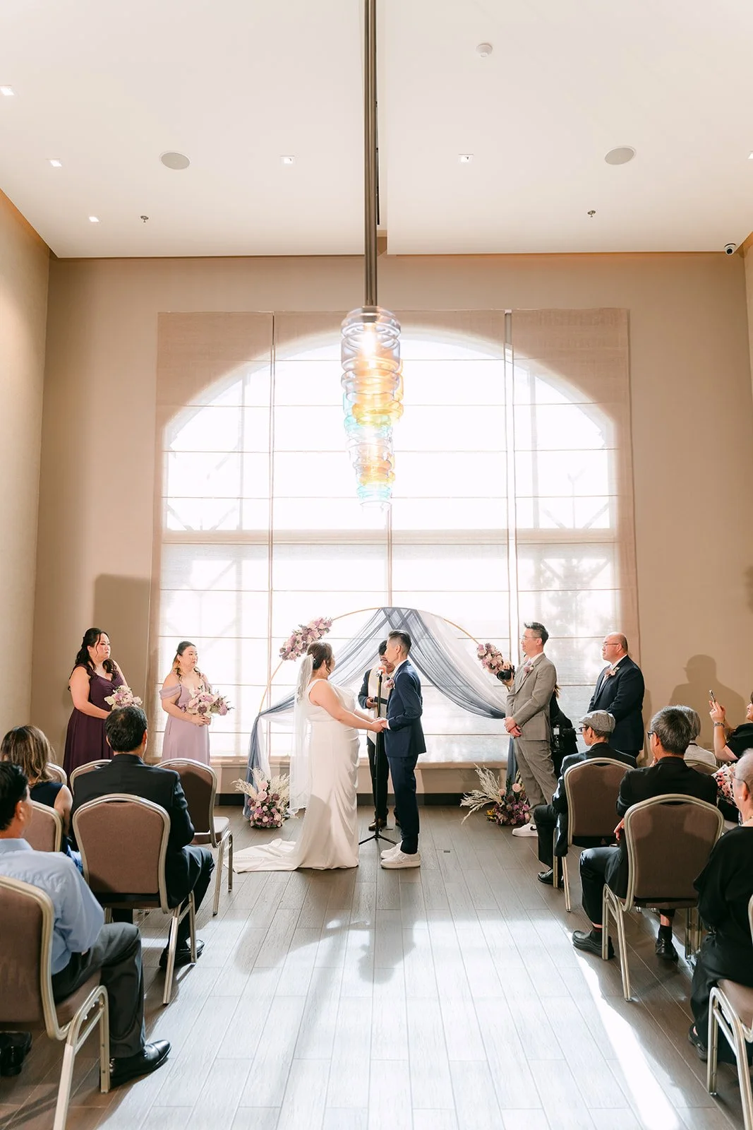 Wide view of the ceremony in front of the arched windows.