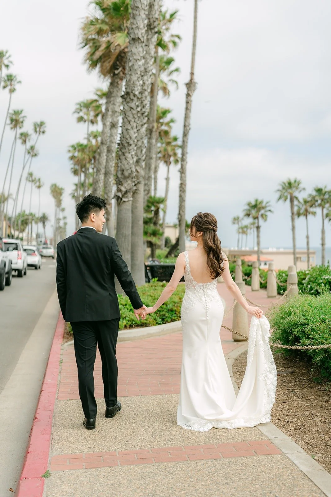 Angela and Eli walking hand in hand along the path toward the palms