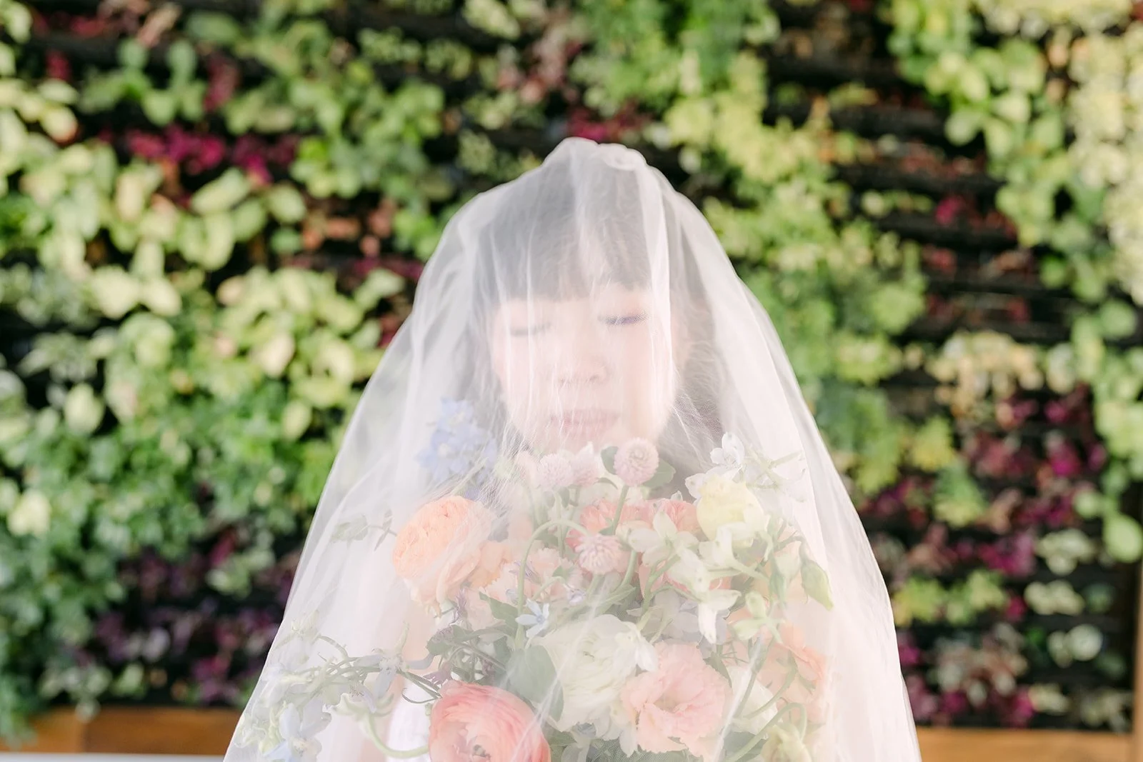 Vivian under her veil holding her bouquet in front of the living wall