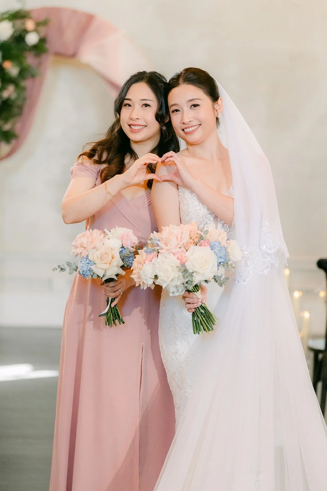 Elisa and a bridesmaid share a hug with their bouquets, photographed by One and Only Production