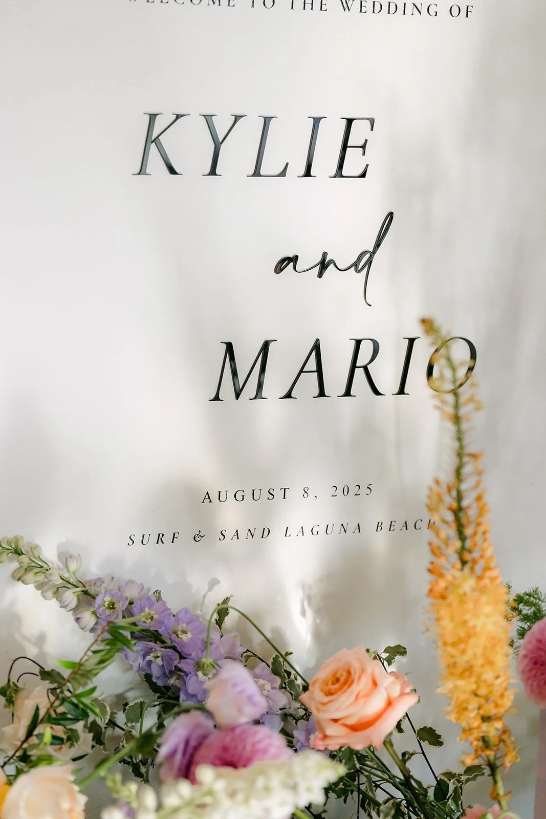 A clear sign reading Kylie and Mario beside a spray of pastel flowers