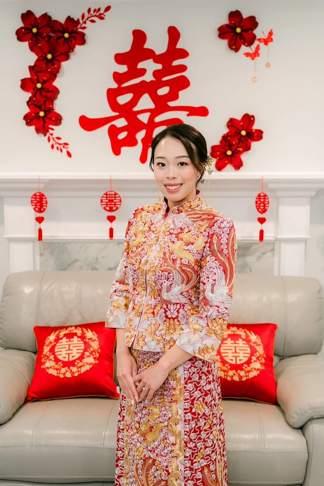 A bride in a gold qun kwa seated on the sofa under double happiness decor.