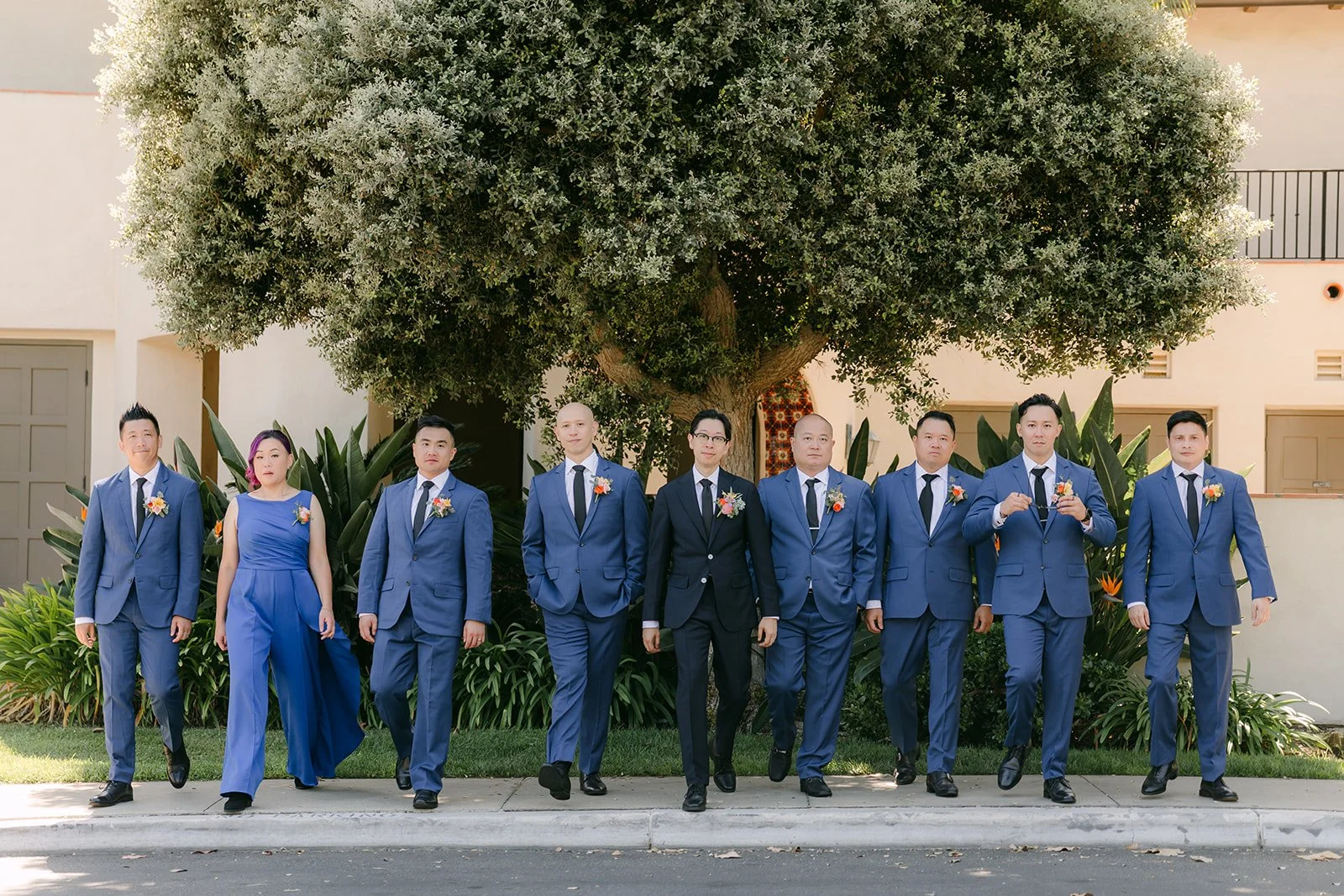 The groomsmen in blue suits lined up beneath the trees
