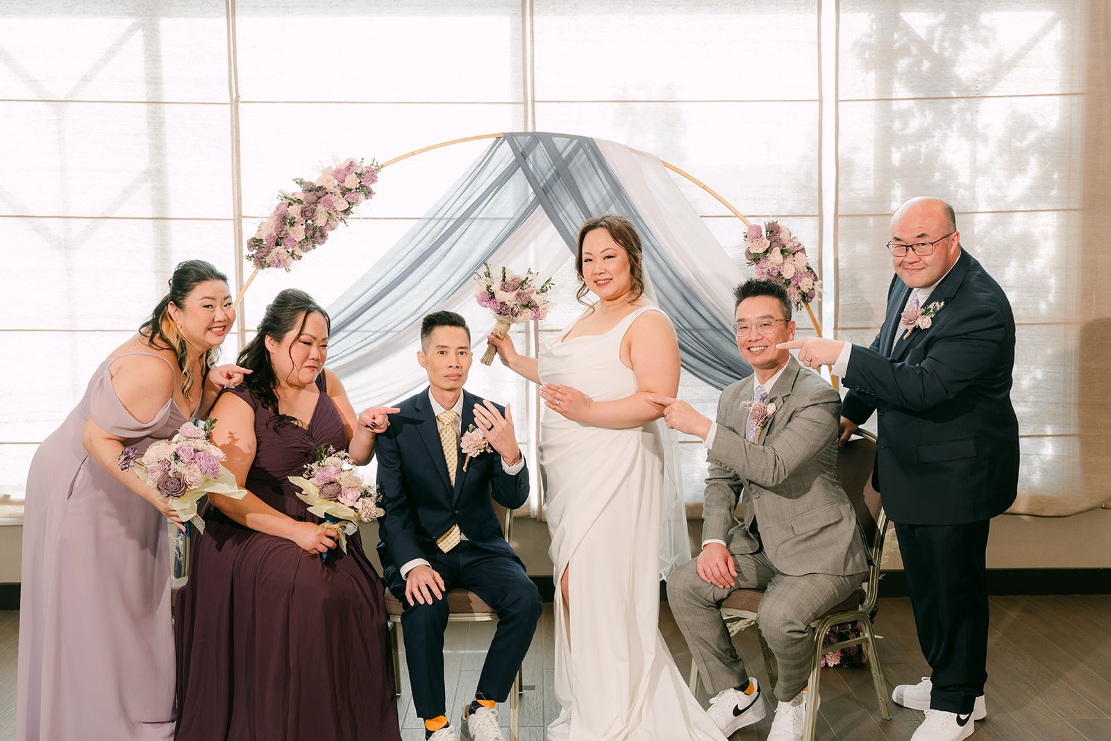 The wedding party laughing at the arch, photographed by One and Only Production.