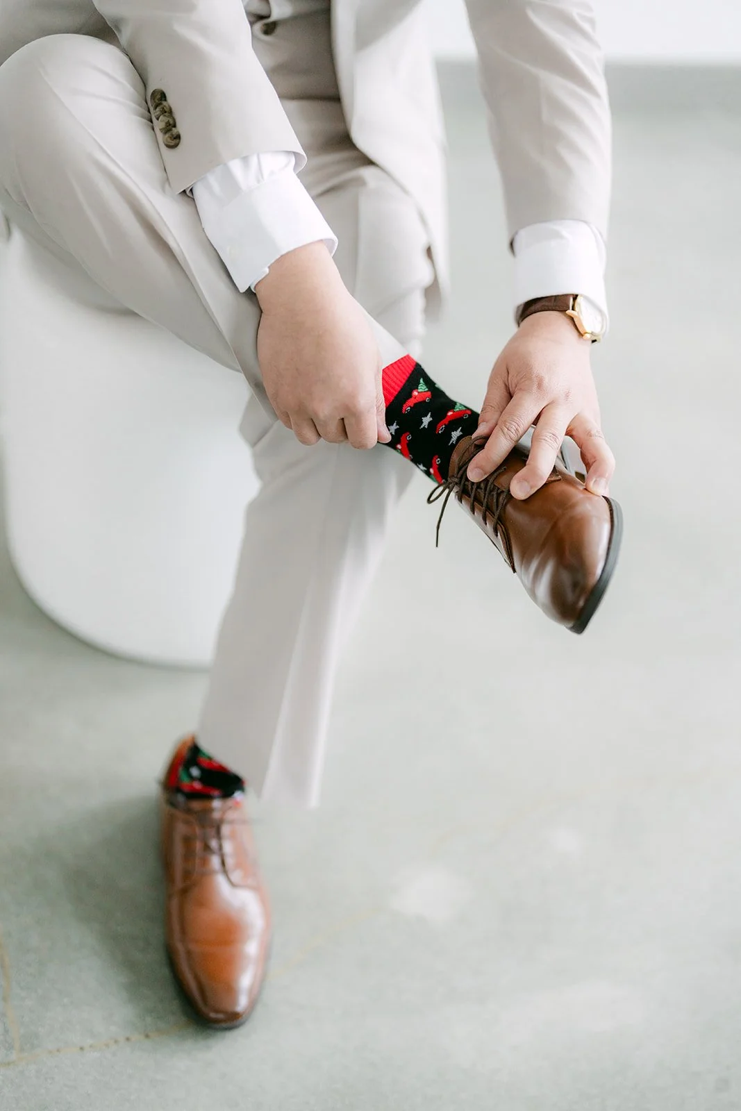 Groom tying brown leather dress shoes with red patterned socks