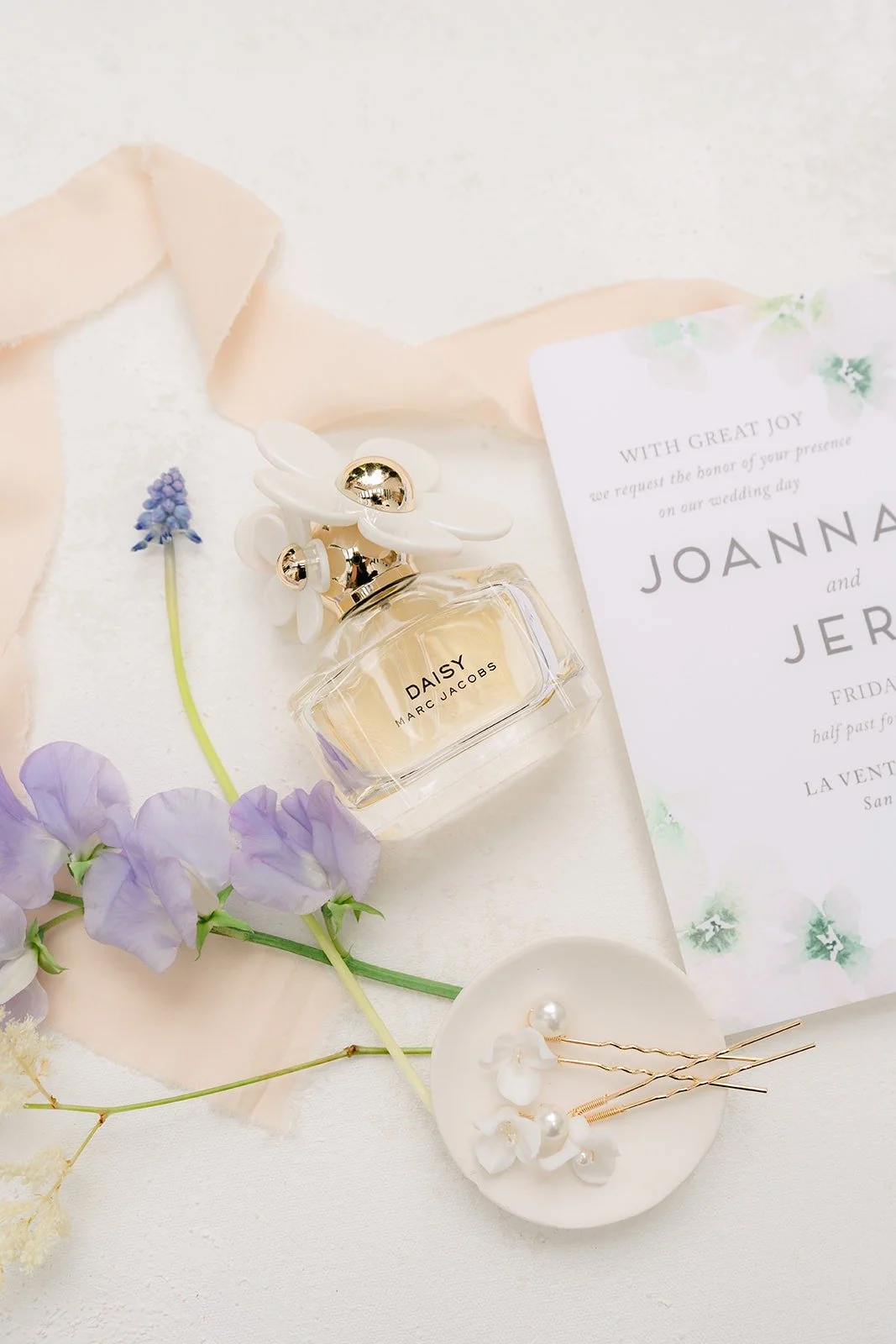 A perfume bottle, hairpiece and invitation styled with sweet peas