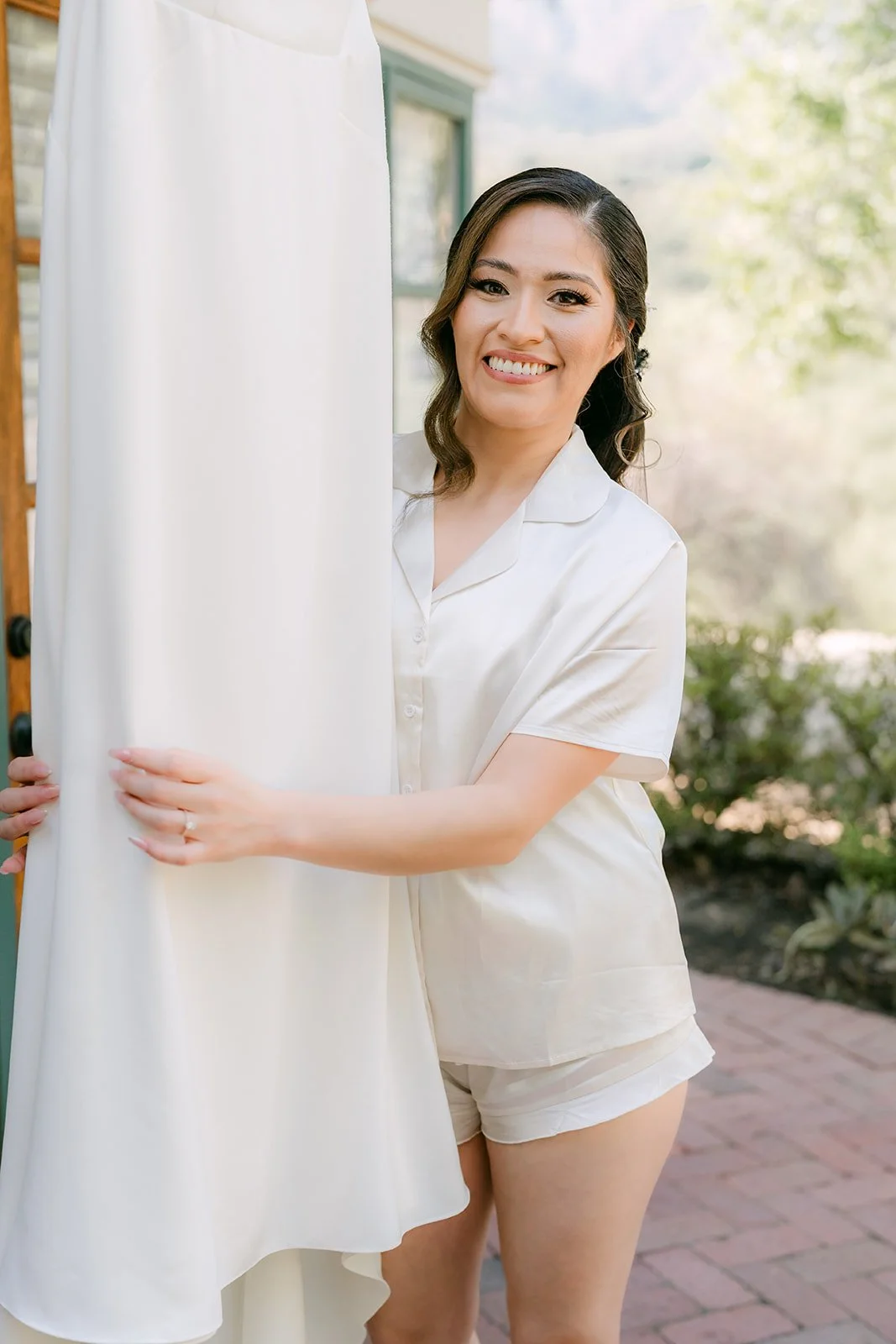Mariana laughing beside her gown on the brick porch