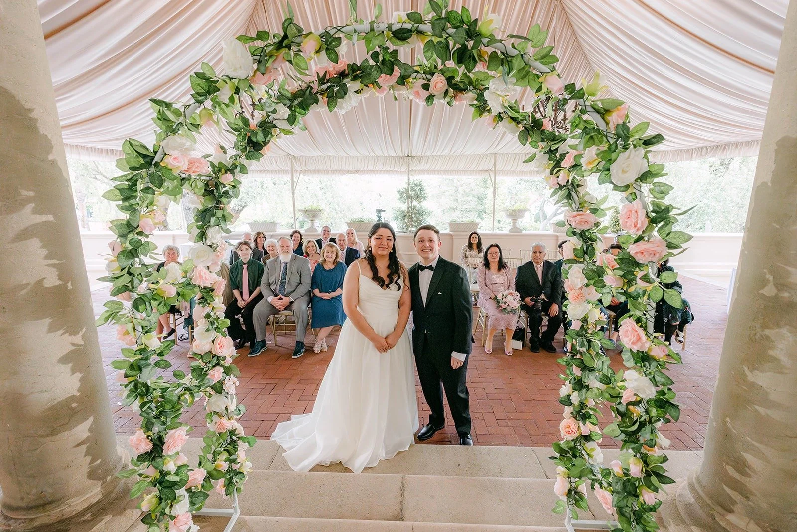 A wide view of Saira and Matthew under the rose arch on the East Patio