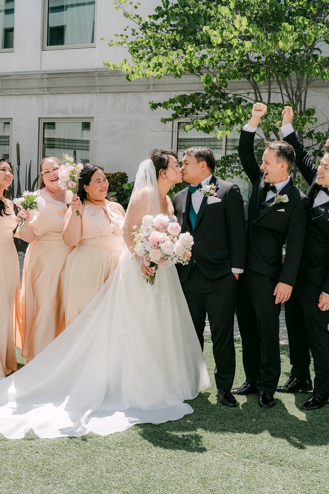 Stella and James kissing in the middle of the wedding party as the groomsmen cheer