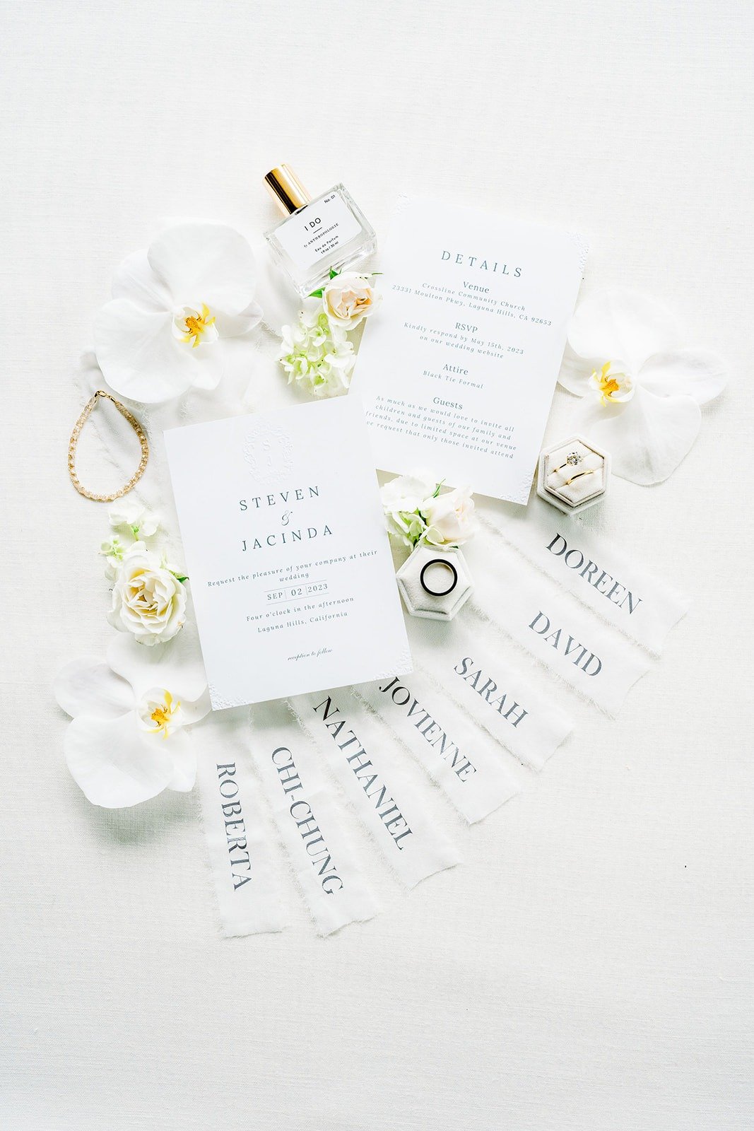 Flat lay of Jacinda and Steven's invitation suite with white orchids and their rings
