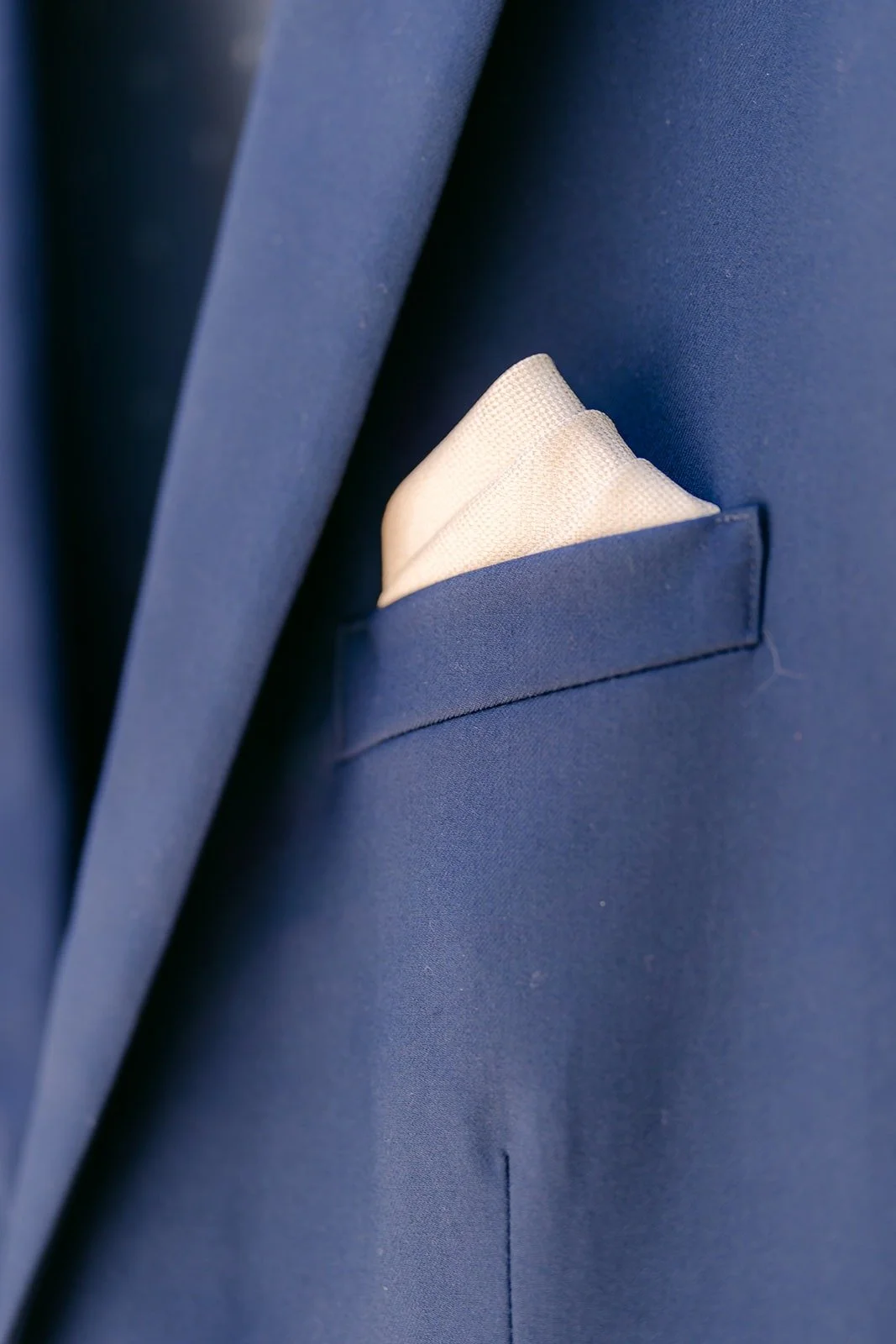 A close view of the folded pocket square on Alex's navy jacket
