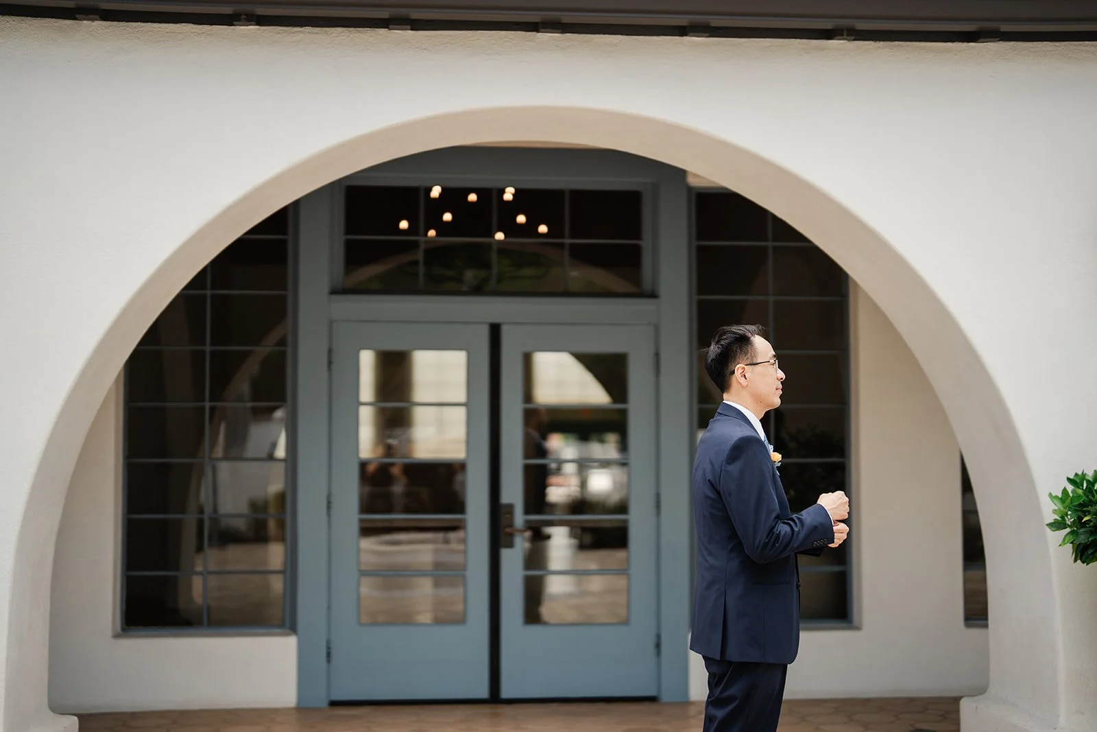 Lawrence waiting under a white arch in the Grand Gimeno courtyard before the first look