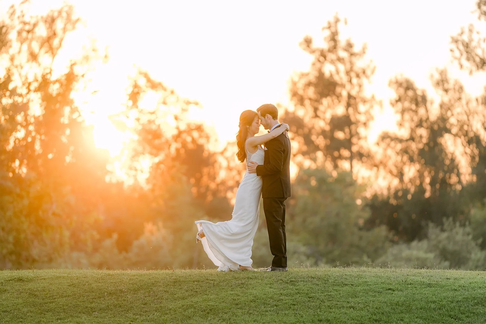 Stephanie and Kevin embracing on the lawn at Sterling Hills as the sun sets behind the trees