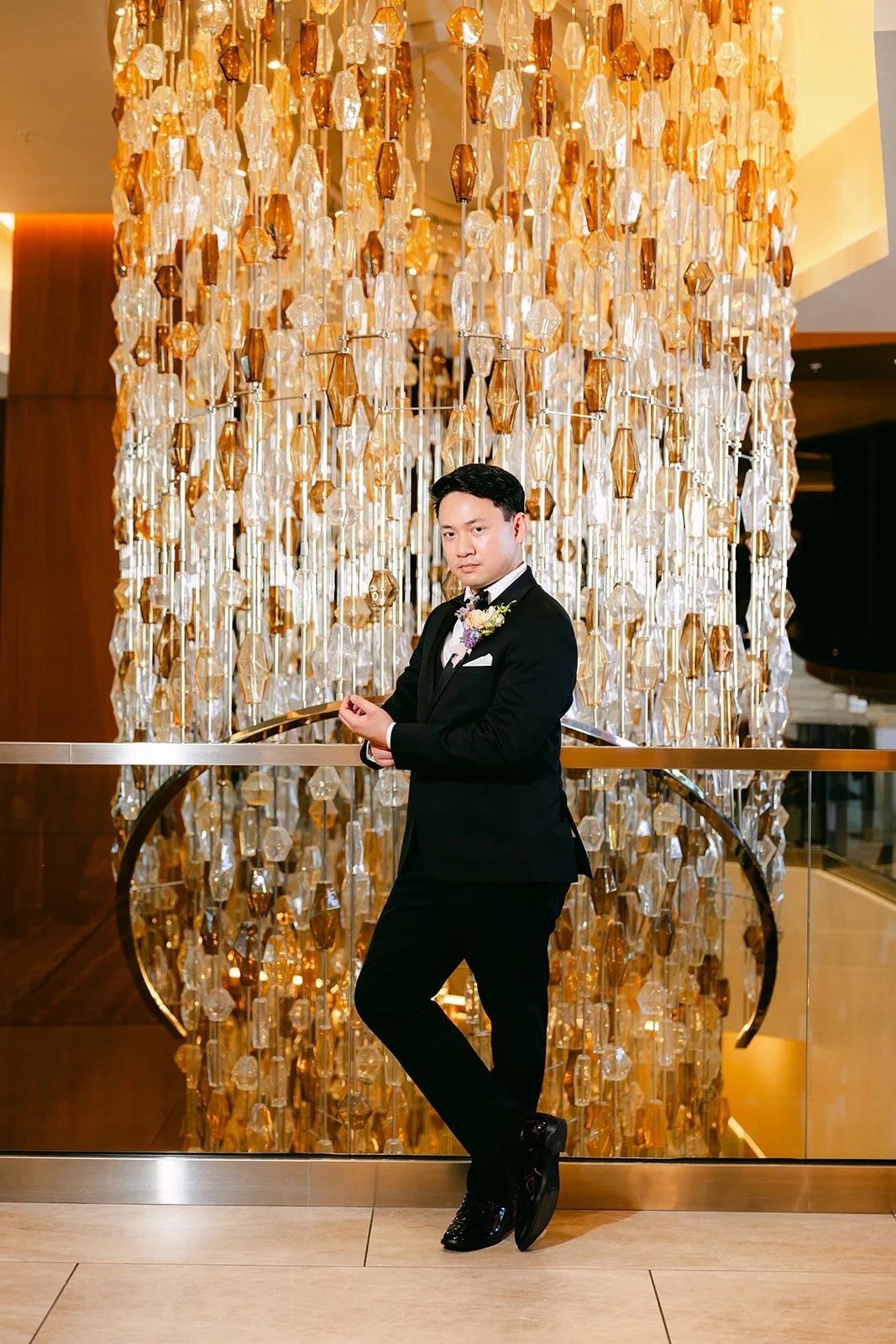 Groom posing in front of the amber chandelier in the JW Marriott Anaheim lobby