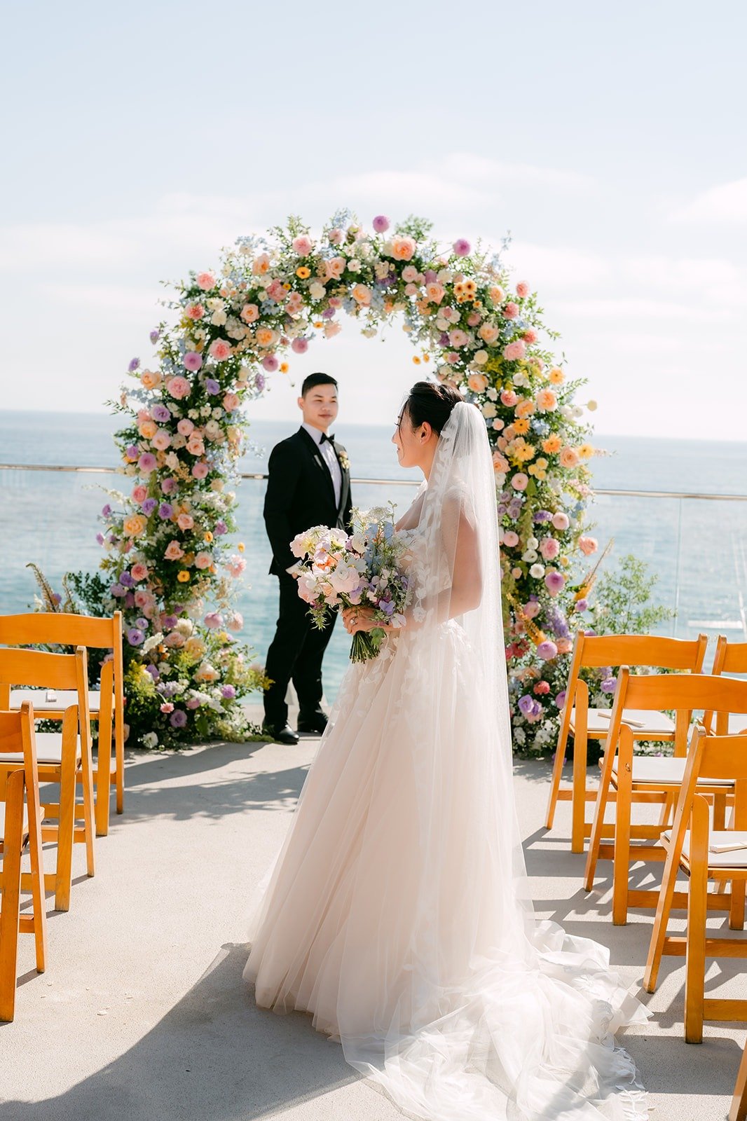 Kylie and Mario standing in the ceremony aisle in front of the arch and the ocean